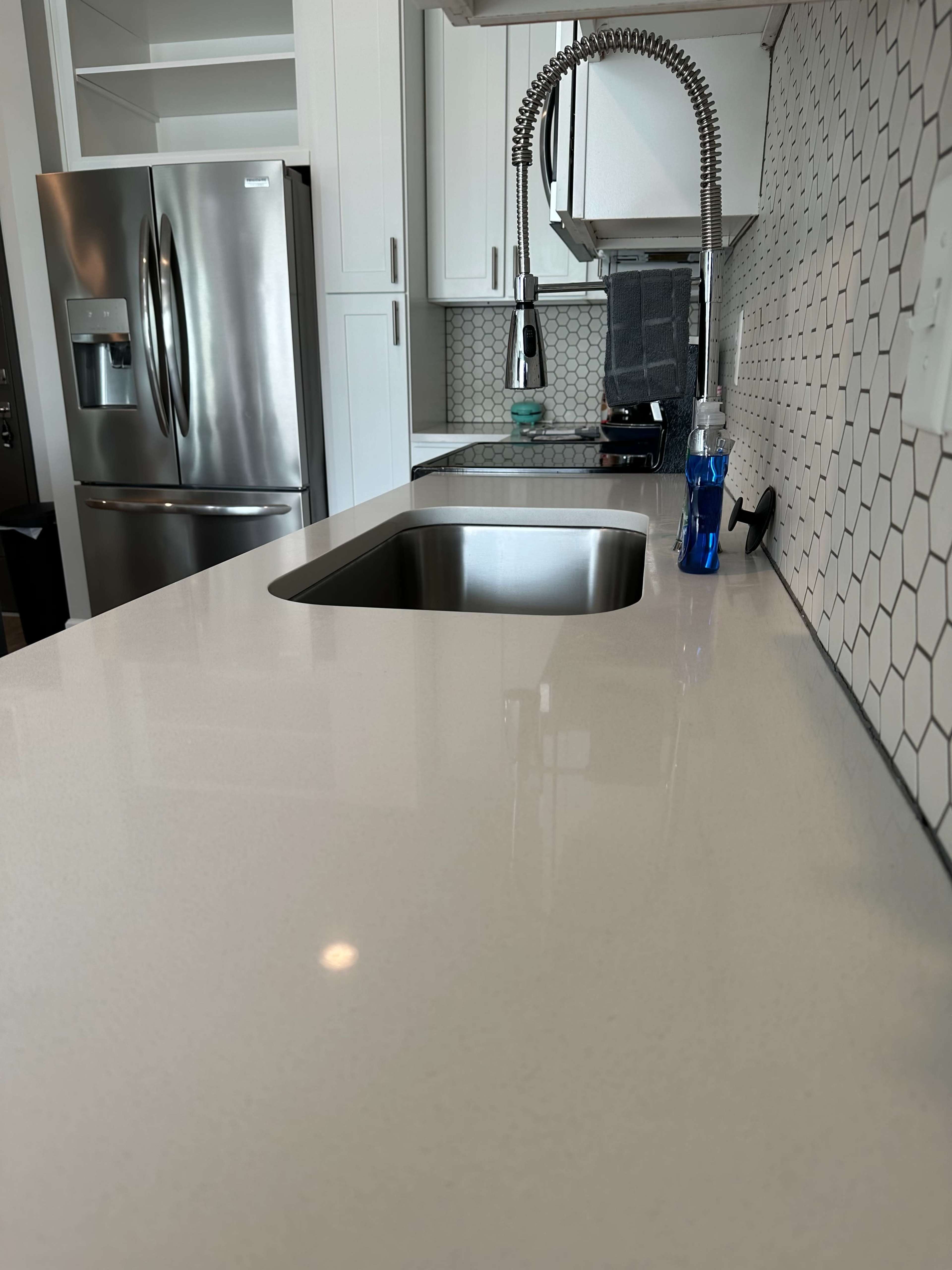 A modern kitchen countertop with a stainless steel sink, a faucet, and a bottle of water beside it.
