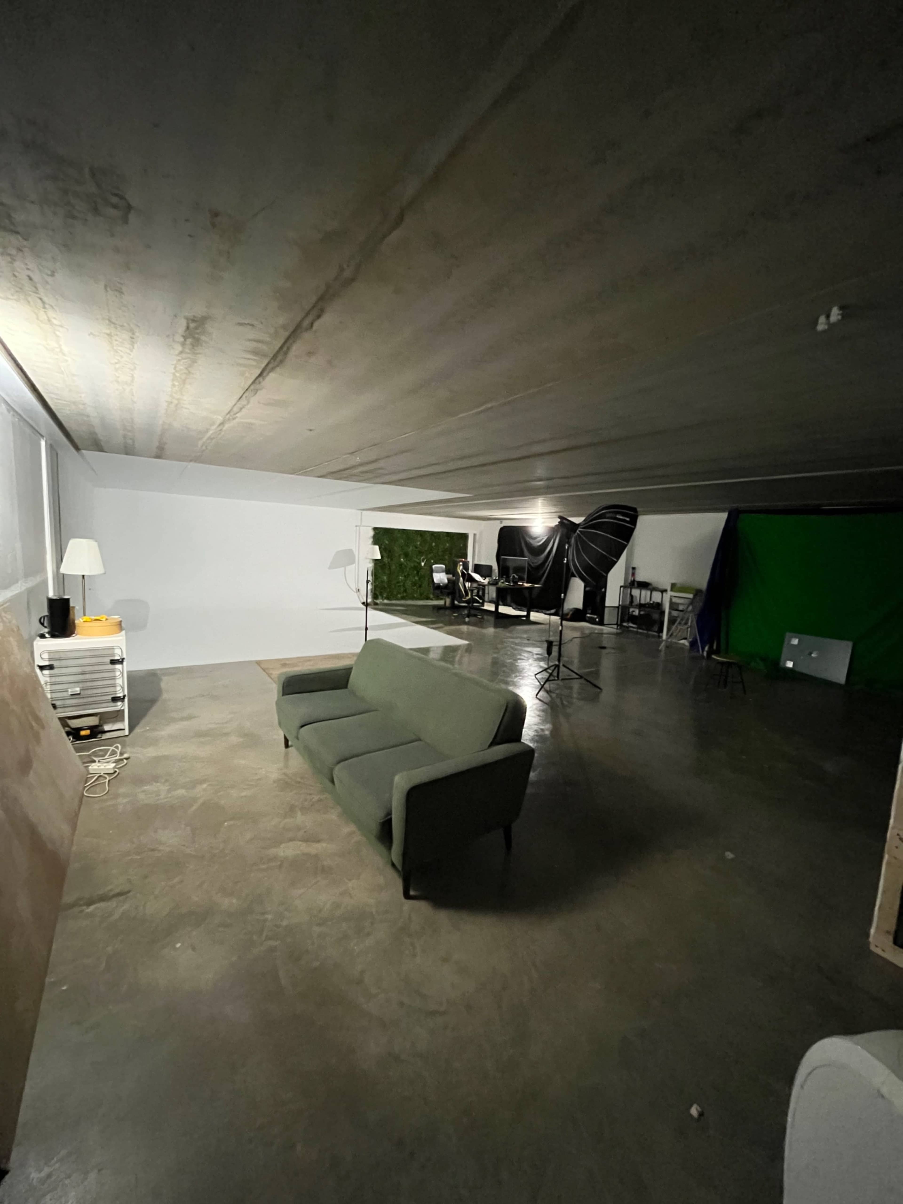 A spacious, empty room with a green couch, a lamp, and a backdrop setup, including a green screen and studio equipment.