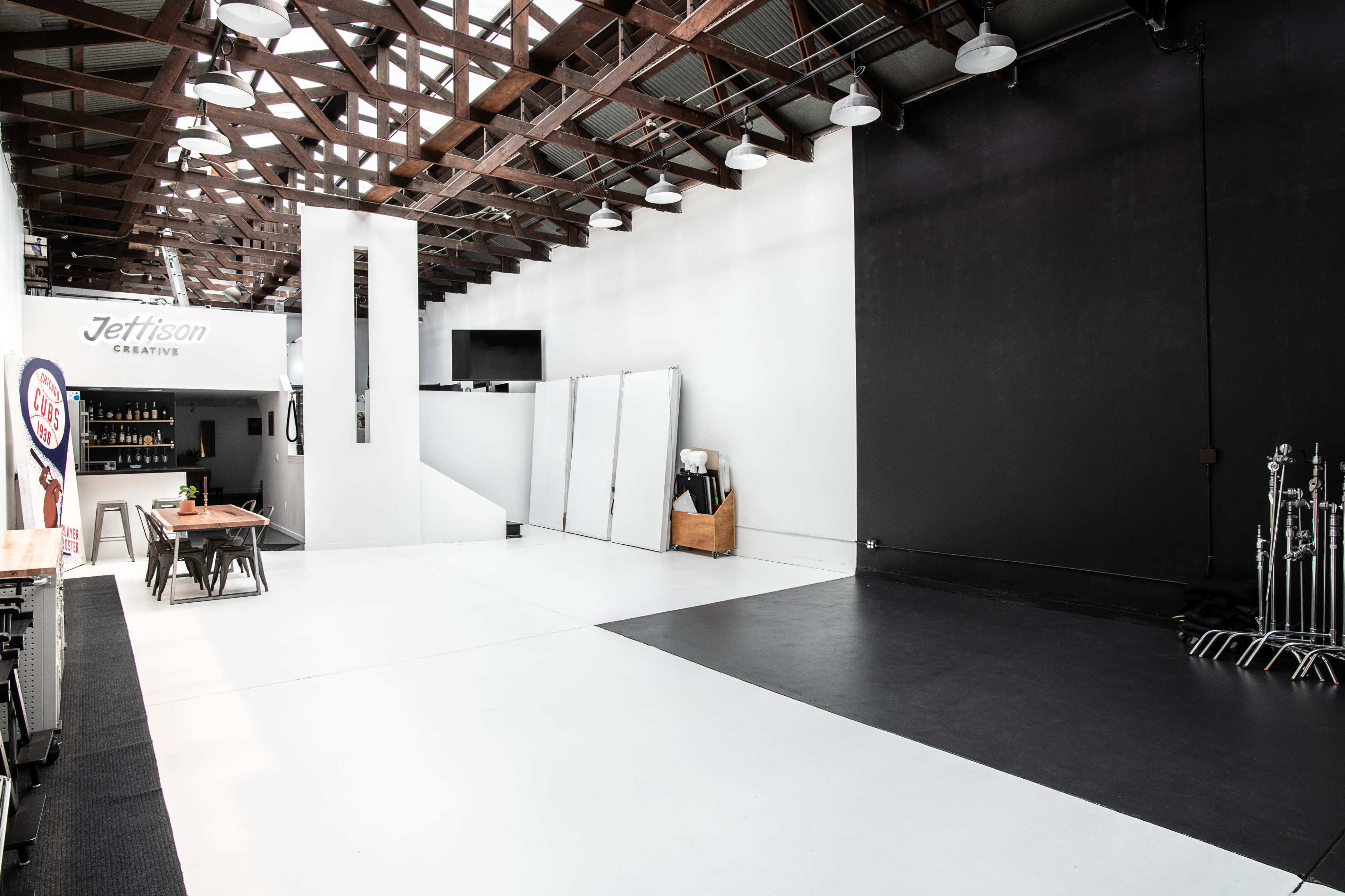 A spacious studio with a white floor, high ceiling, and a black wall, featuring minimalist furniture and equipment.