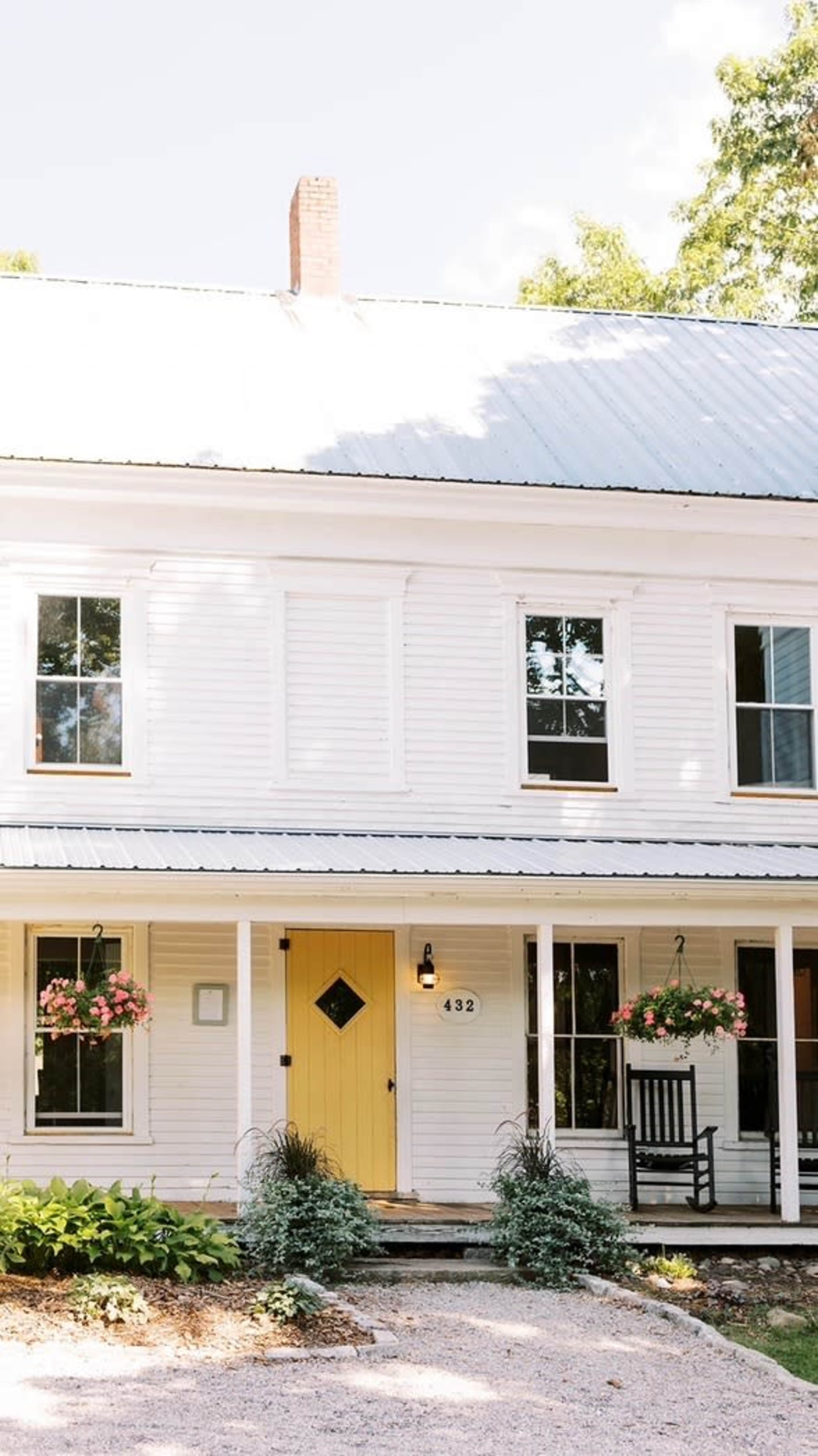 A two-story white house with a yellow front door, surrounded by green landscaping and flower baskets.