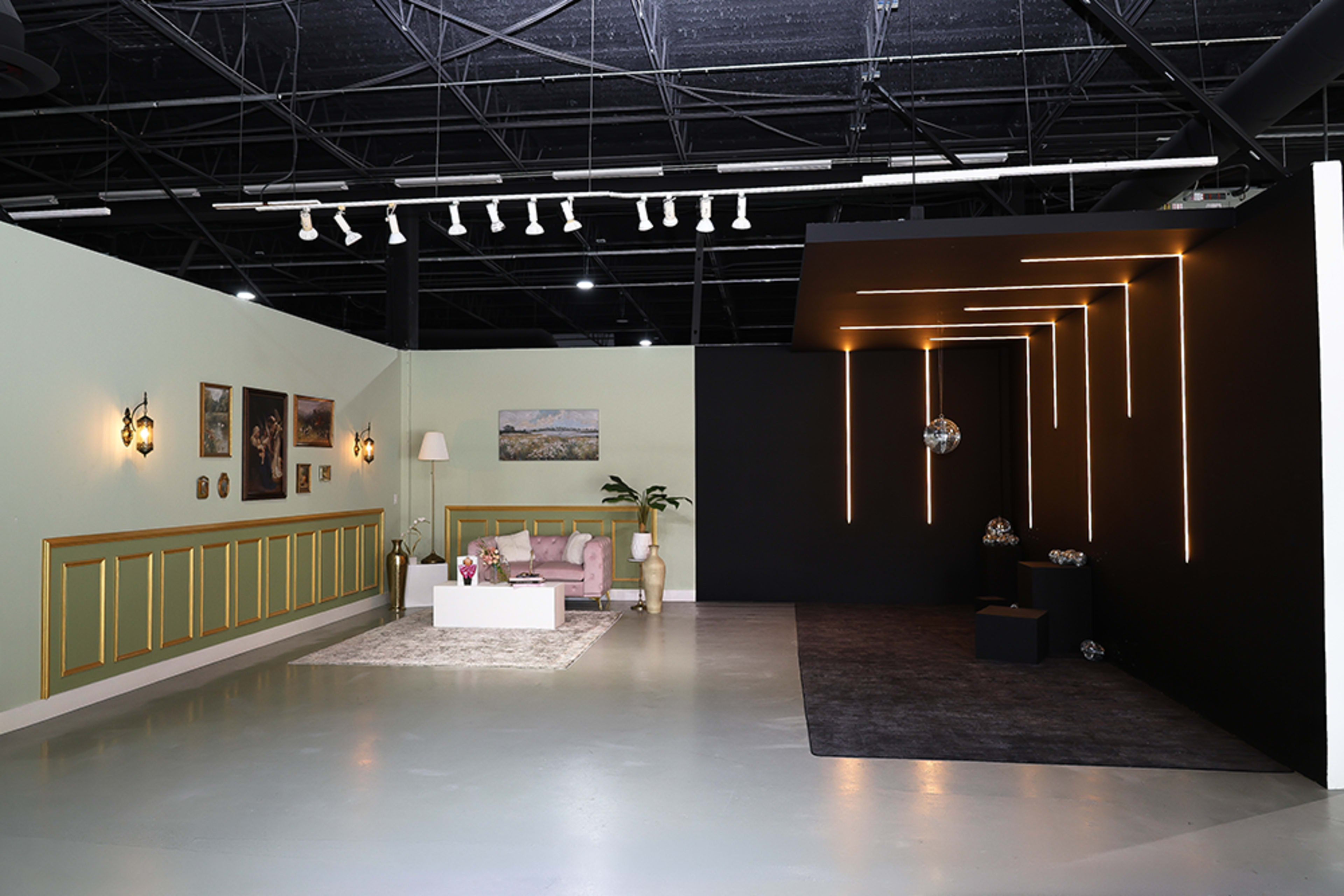 The image shows a spacious studio with a light-colored seating area on one side and a dark section featuring hanging light fixtures on the other.