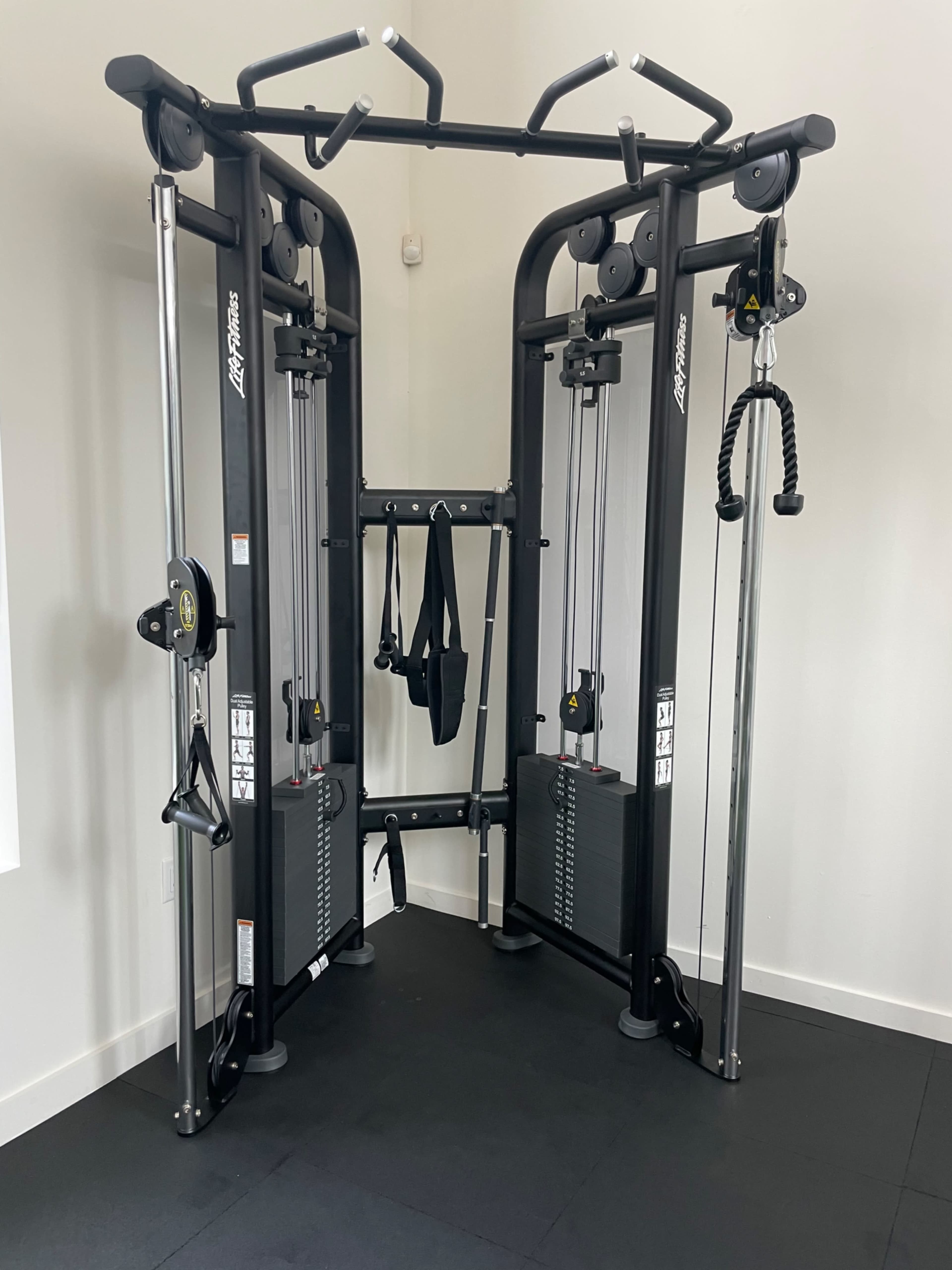 A dual cable machine with adjustable pulleys and weight stacks positioned in a fitness room.