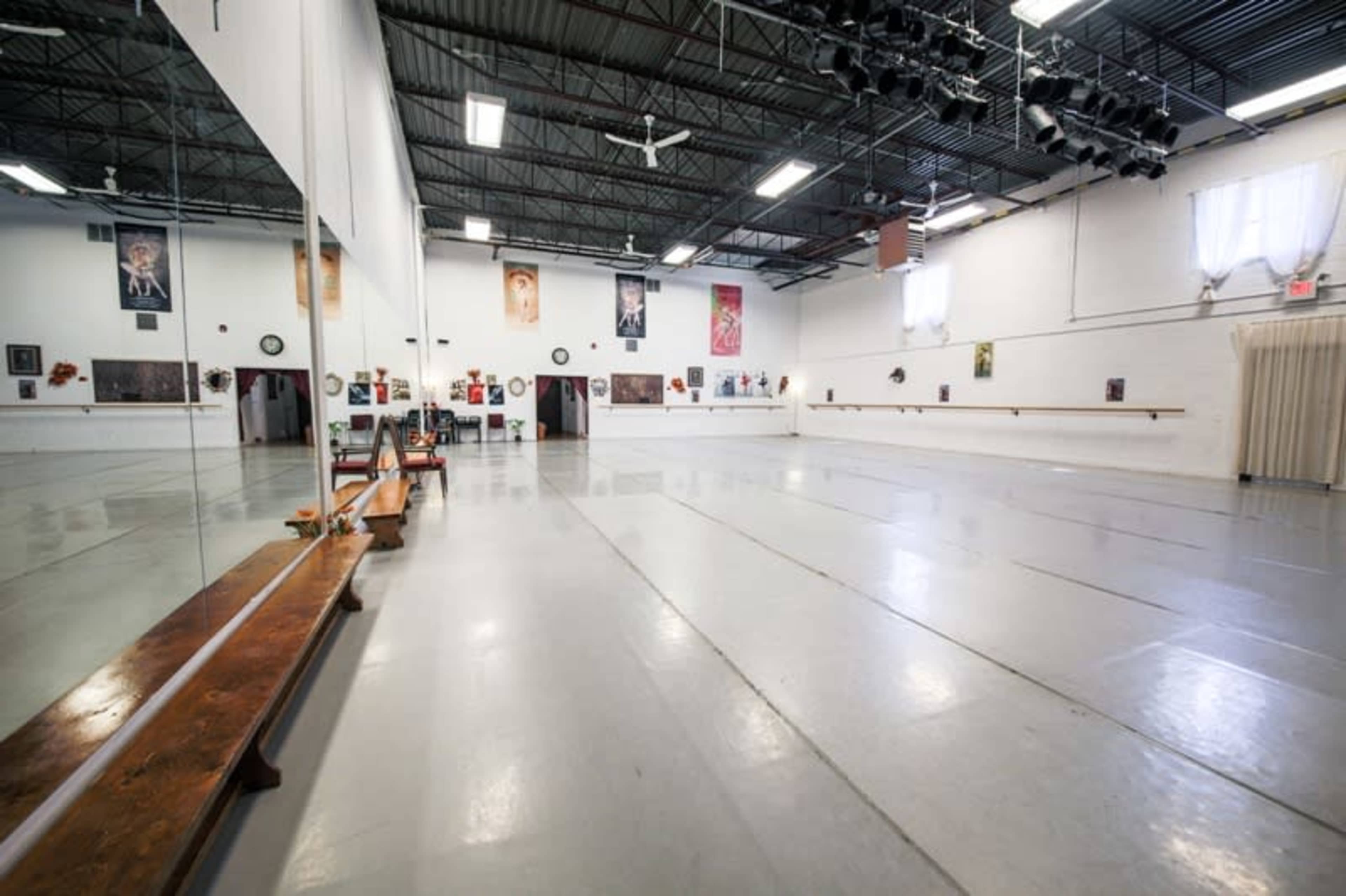 A spacious dance studio with mirrors, a wooden ballet bar, and framed photographs on the walls.