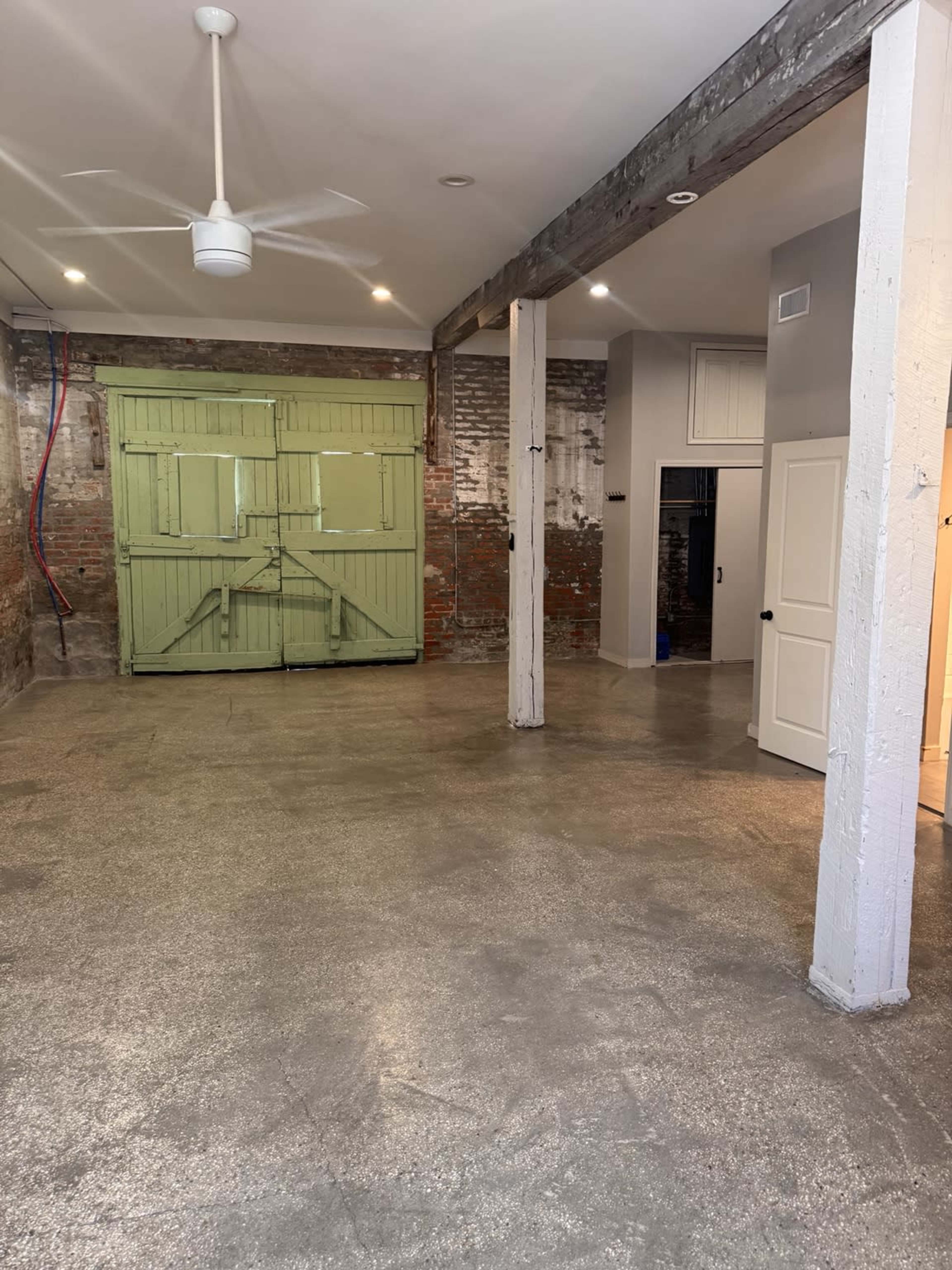 The image shows an empty room with concrete flooring, exposed brick walls, and a large green door against one wall.