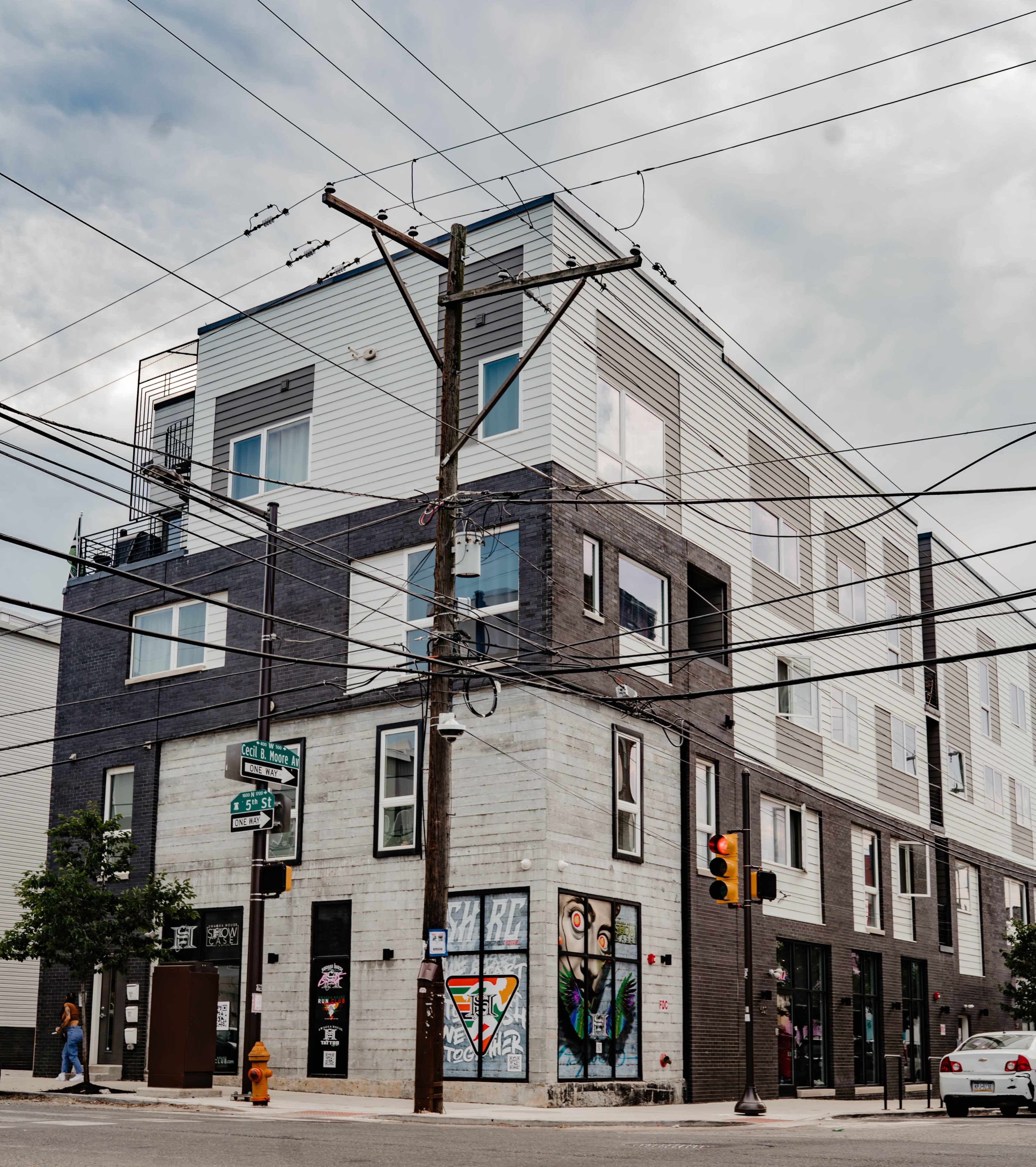 A modern multi-story building with a combination of gray and white facades is located at an intersection, prominently featuring street art and utility poles with overhead wires.