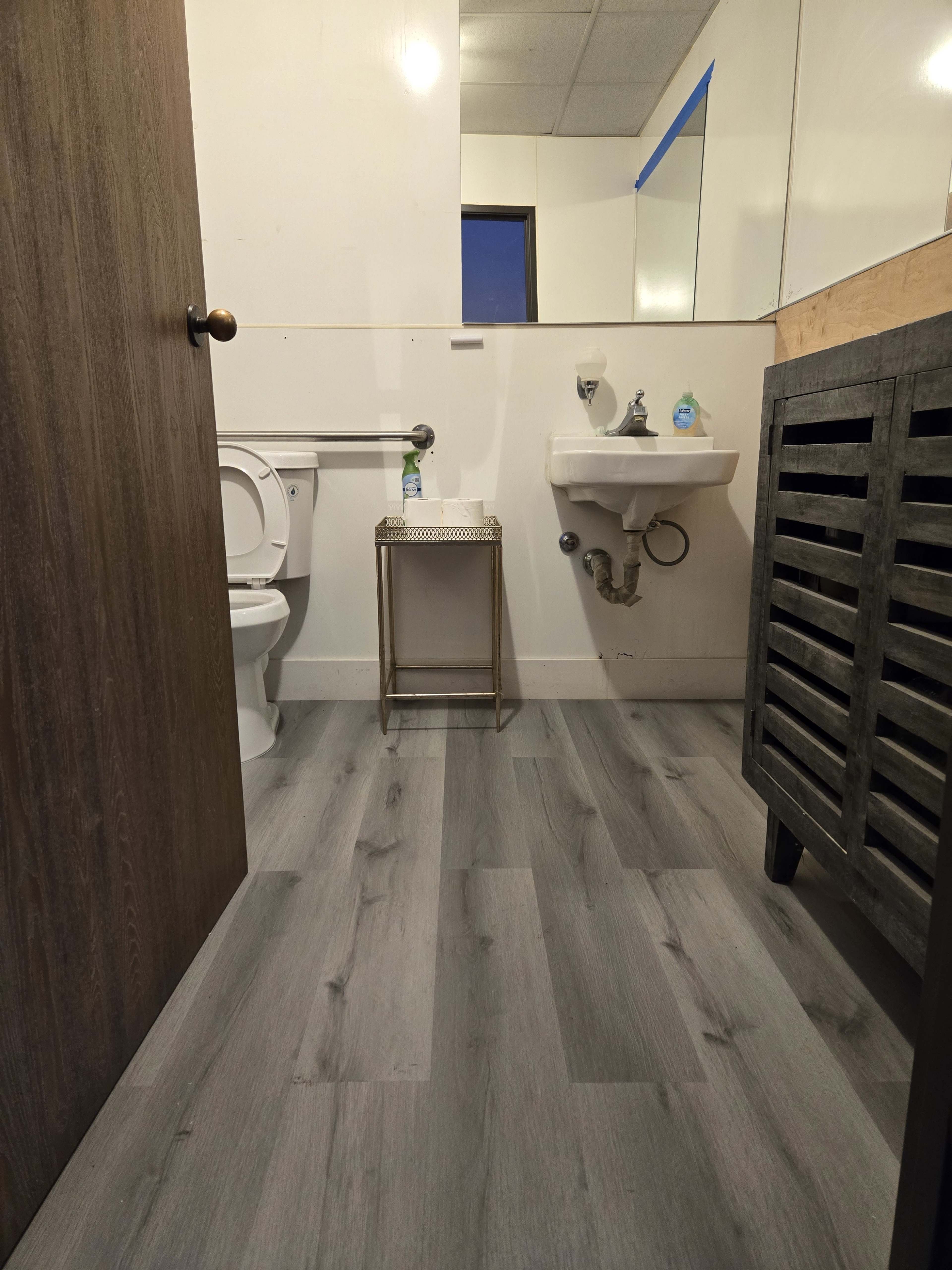 A small bathroom with a toilet, a sink, a metal table, and gray wooden flooring.