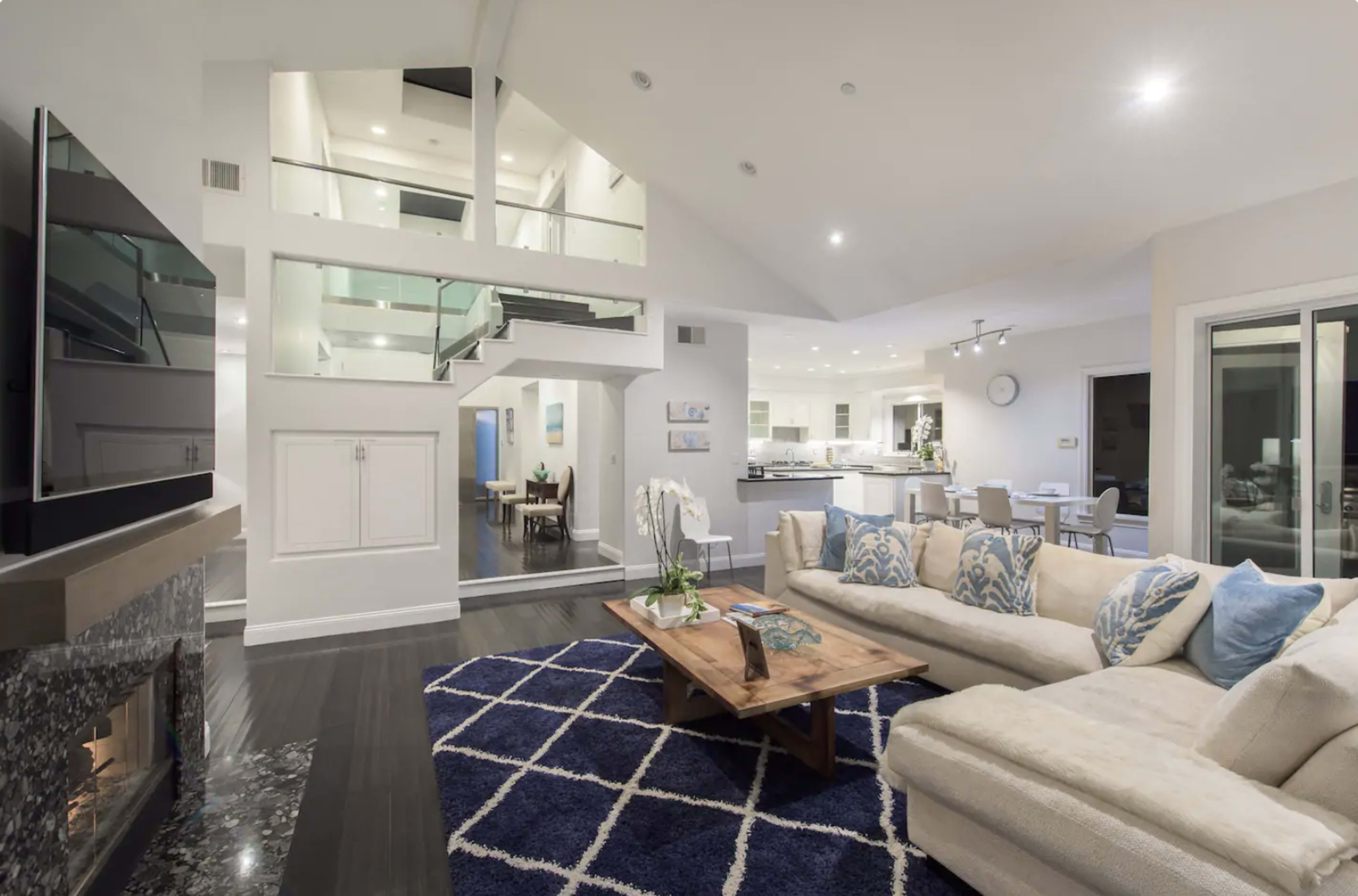The living area features a sectional sofa arranged around a wooden coffee table, with a modern fireplace and a staircase leading to the upper level, all illuminated by overhead lights.