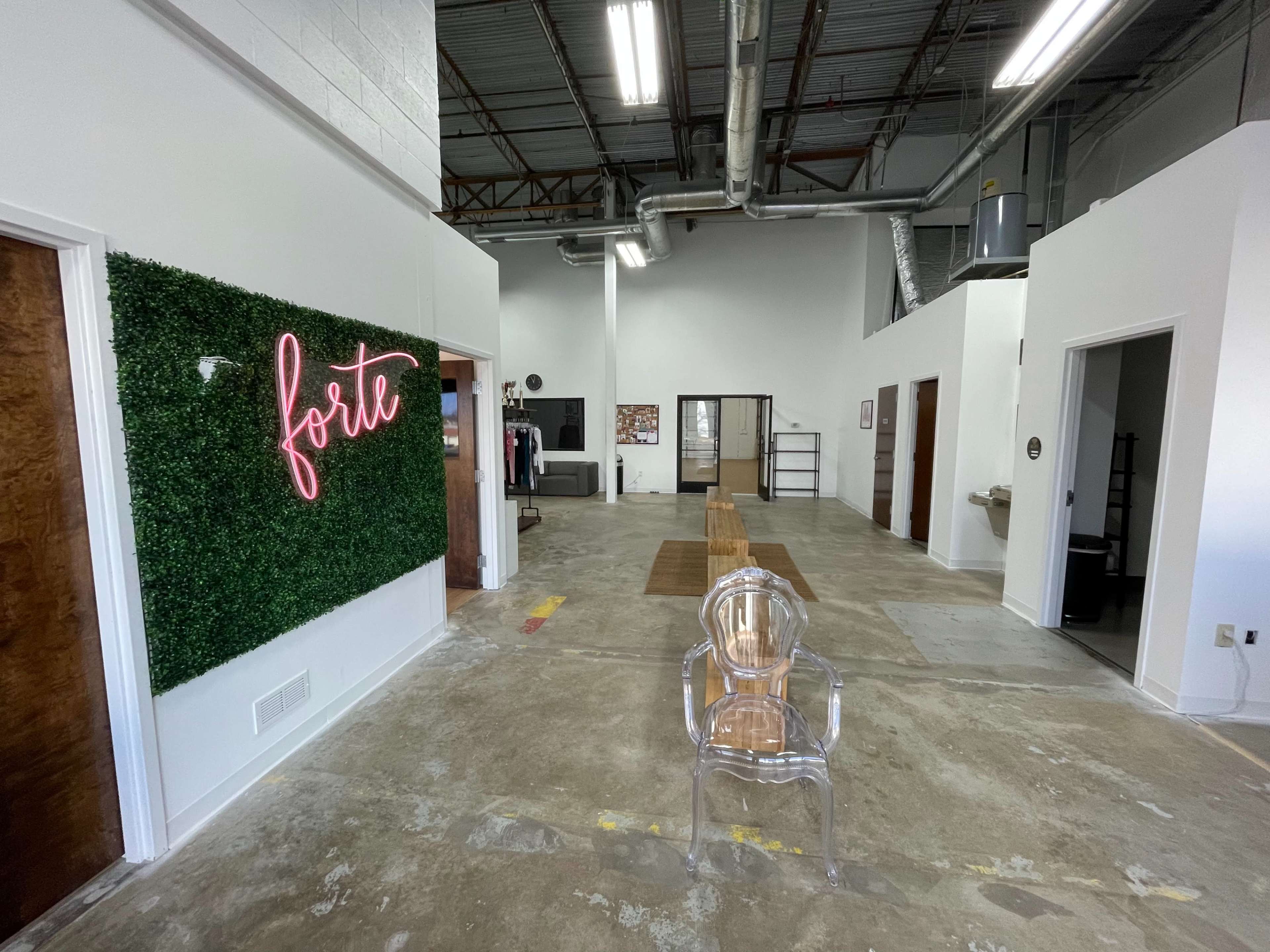 A spacious, modern interior with a green wall featuring the word "forte" in neon lights, and several doorways leading to other rooms.