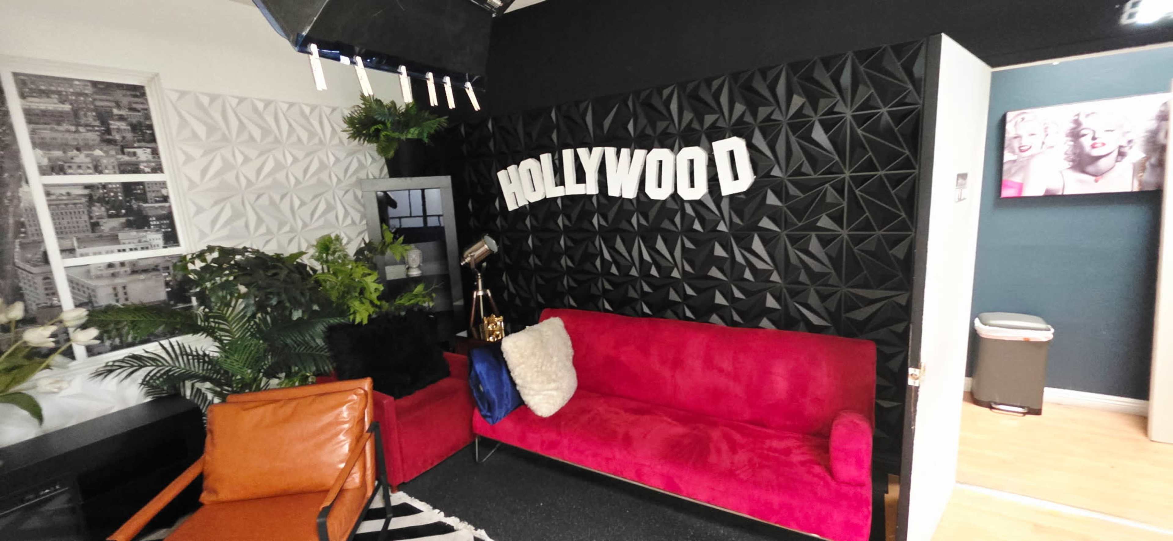 The image shows a stylish interior with a pink couch, an orange chair, geometric wall designs, and the word "HOLLYWOOD" prominently displayed.
