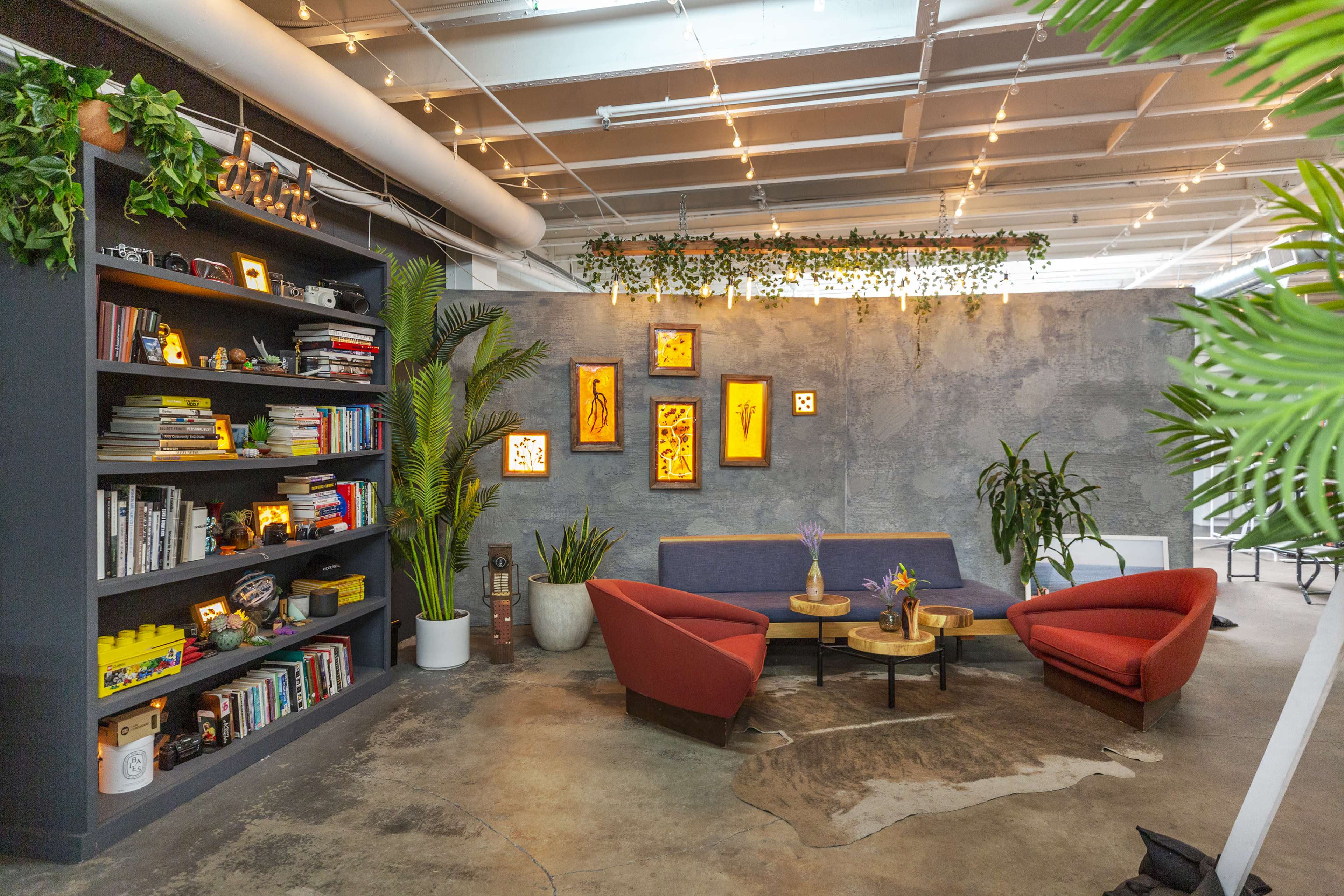 A stylish interior features a living area with two red chairs, a blue sofa, a bookshelf filled with books, and framed artwork on a textured wall.