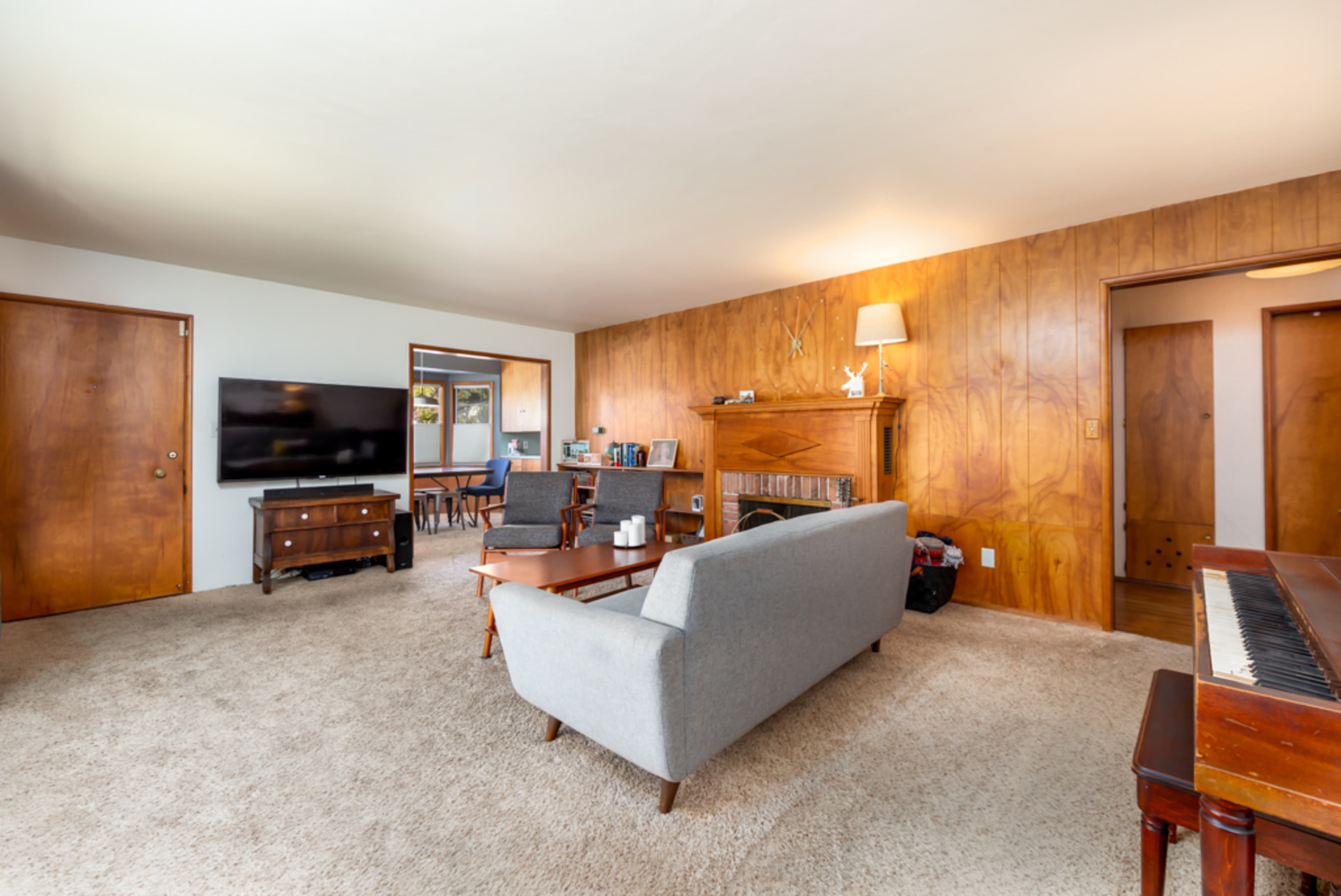 The living room features a gray sofa, a coffee table, a television on a wooden cabinet, and wood-paneled walls.