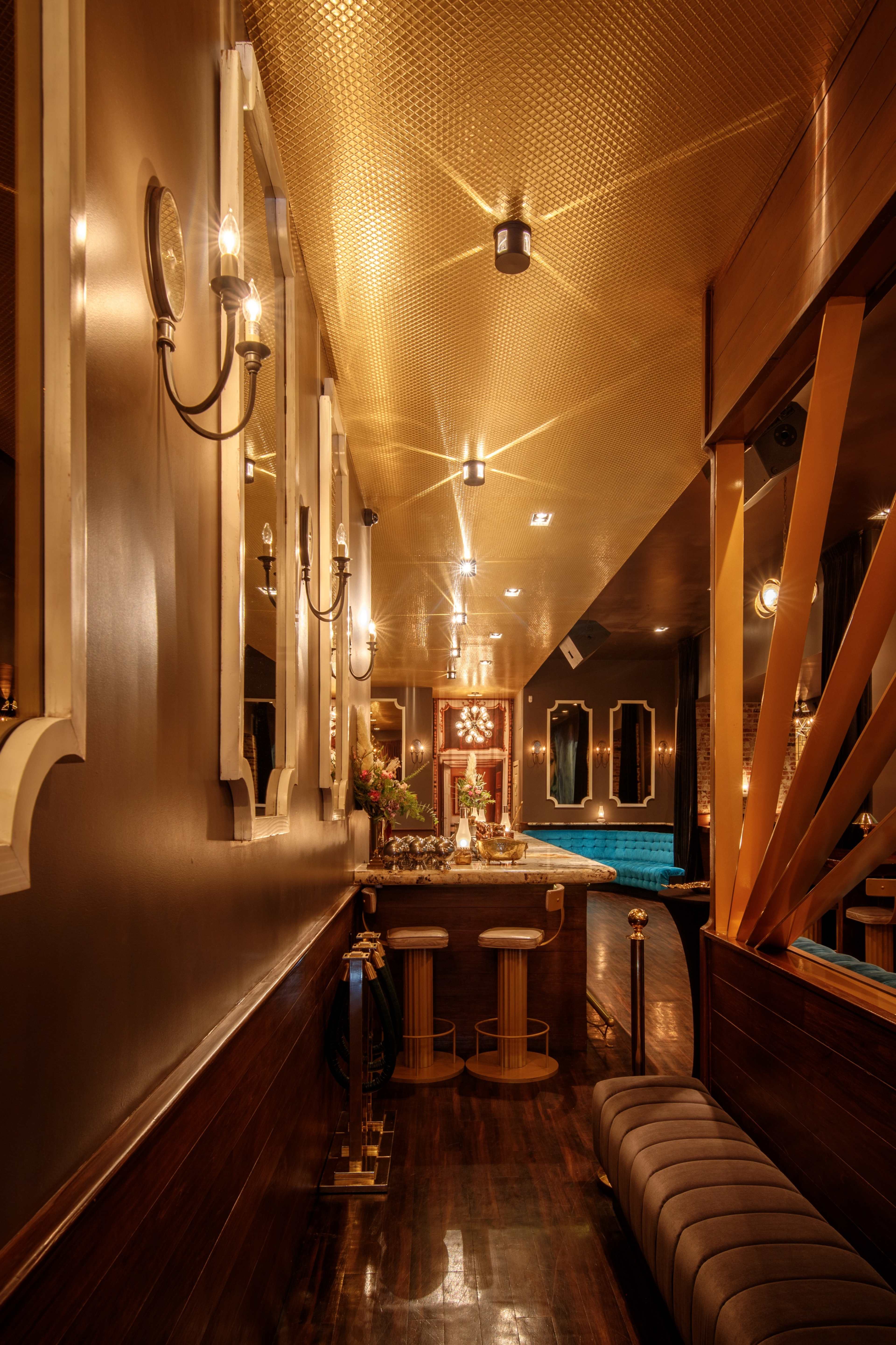 A dimly lit lounge with golden accents, featuring a bar area and decorative mirrors along the walls.