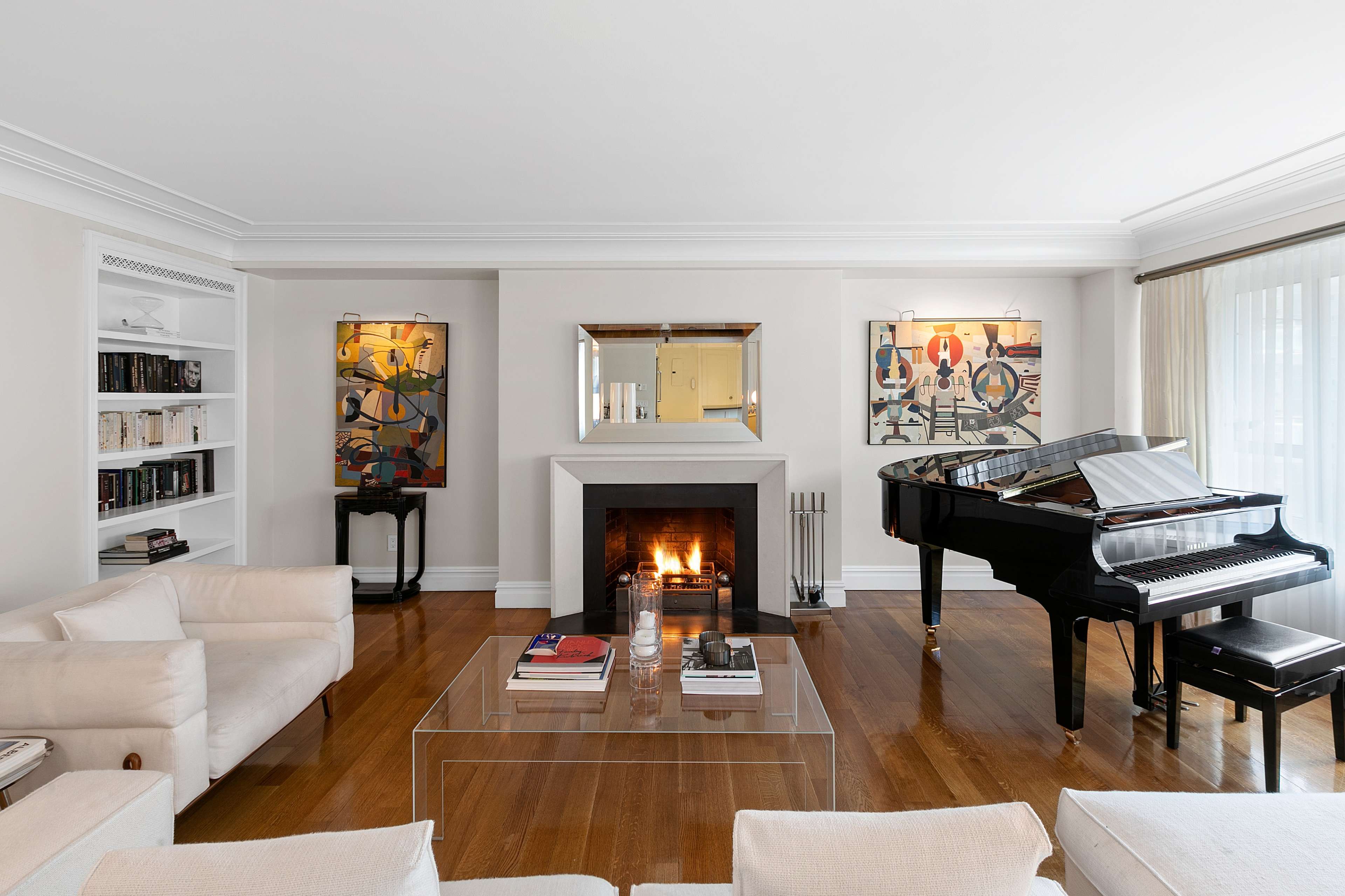 A living room featuring a fireplace, a grand piano, bookshelves, and framed artwork on the walls.