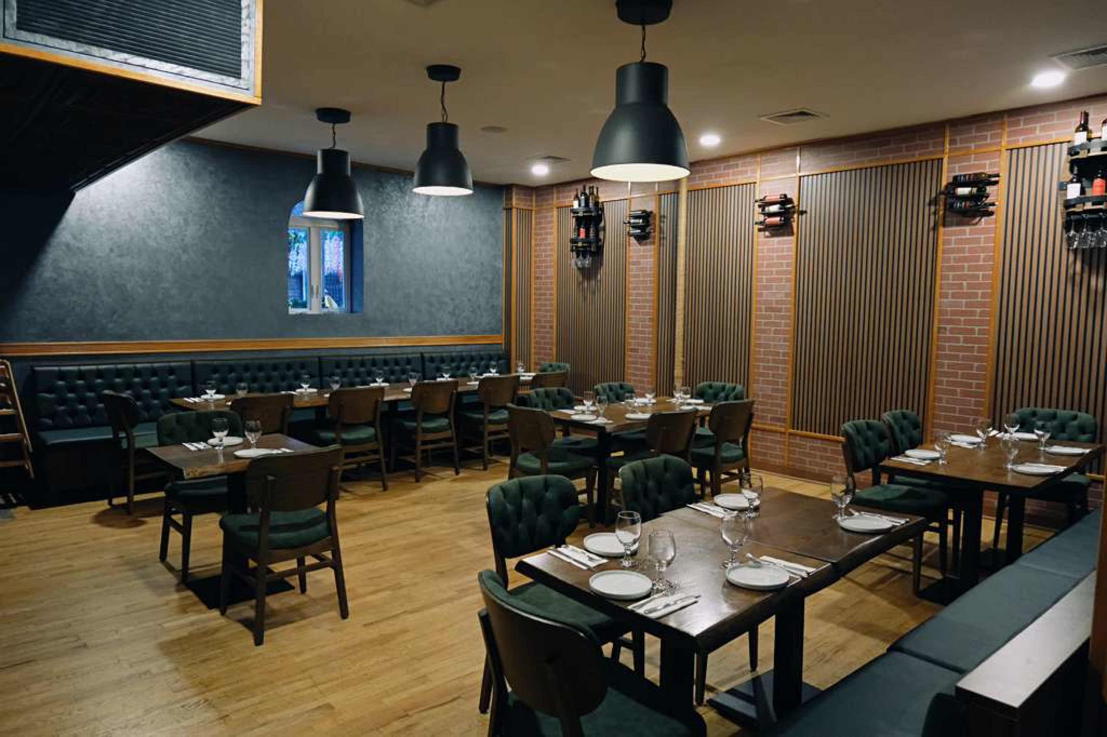 The image shows a spacious restaurant interior with wooden flooring, dark green upholstered seating, and tables set with plates and cutlery.