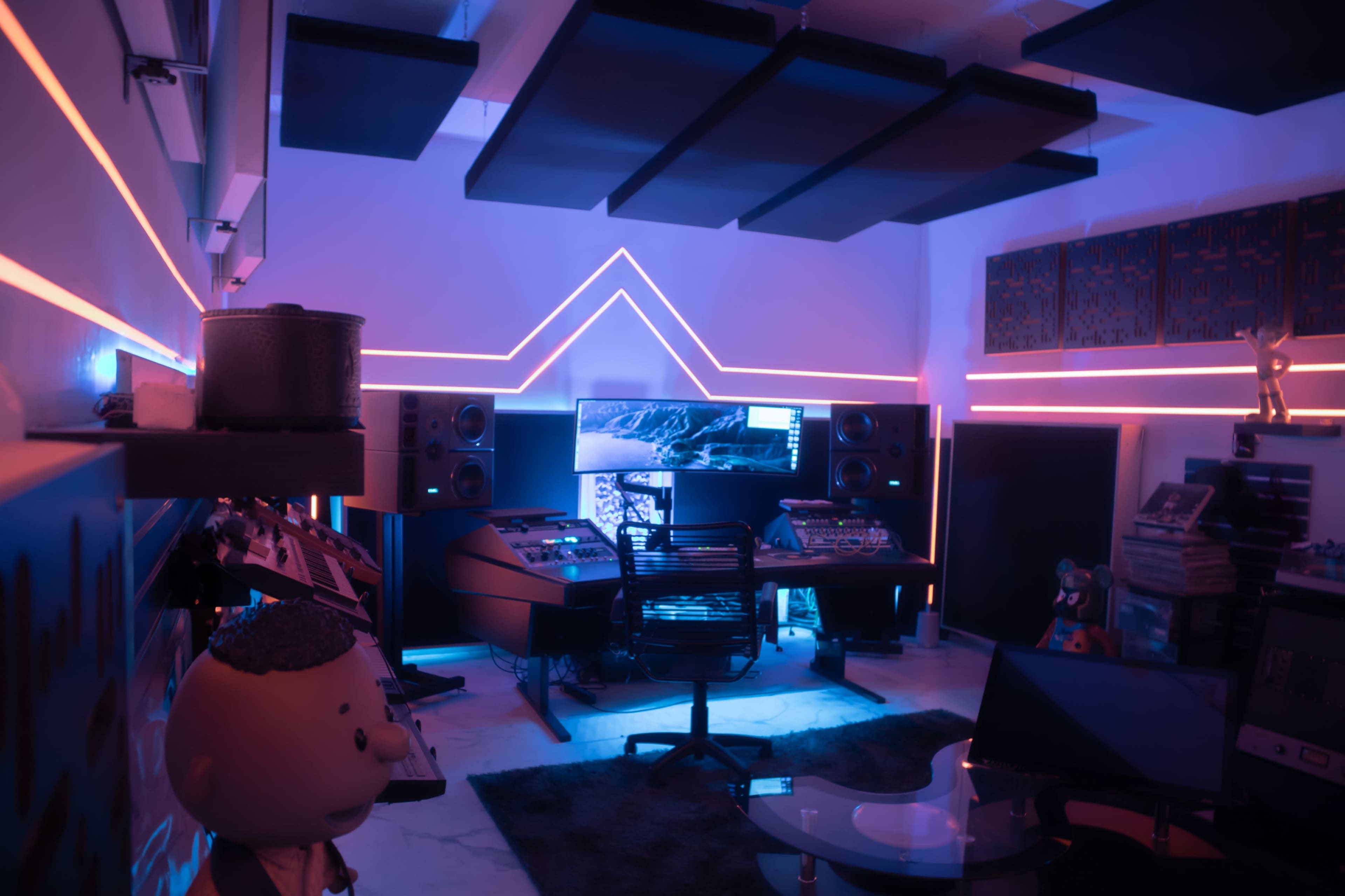 The image shows a modern music studio with neon lighting, featuring a central mixing console and multiple speakers, surrounded by soundproofing panels.