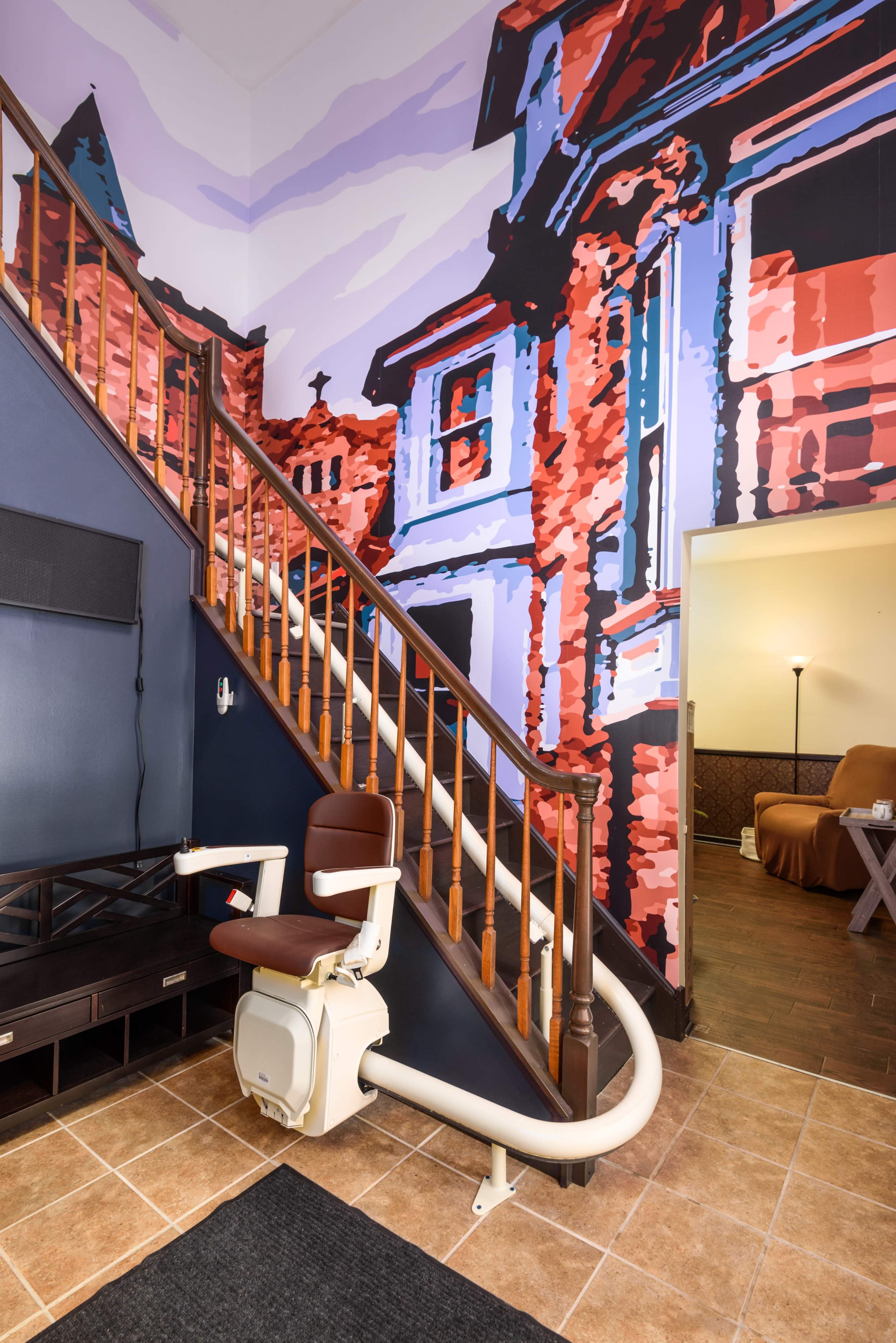 A staircase with a decorative mural on the wall, featuring a colorful depiction of buildings, and a stairlift positioned alongside the steps.