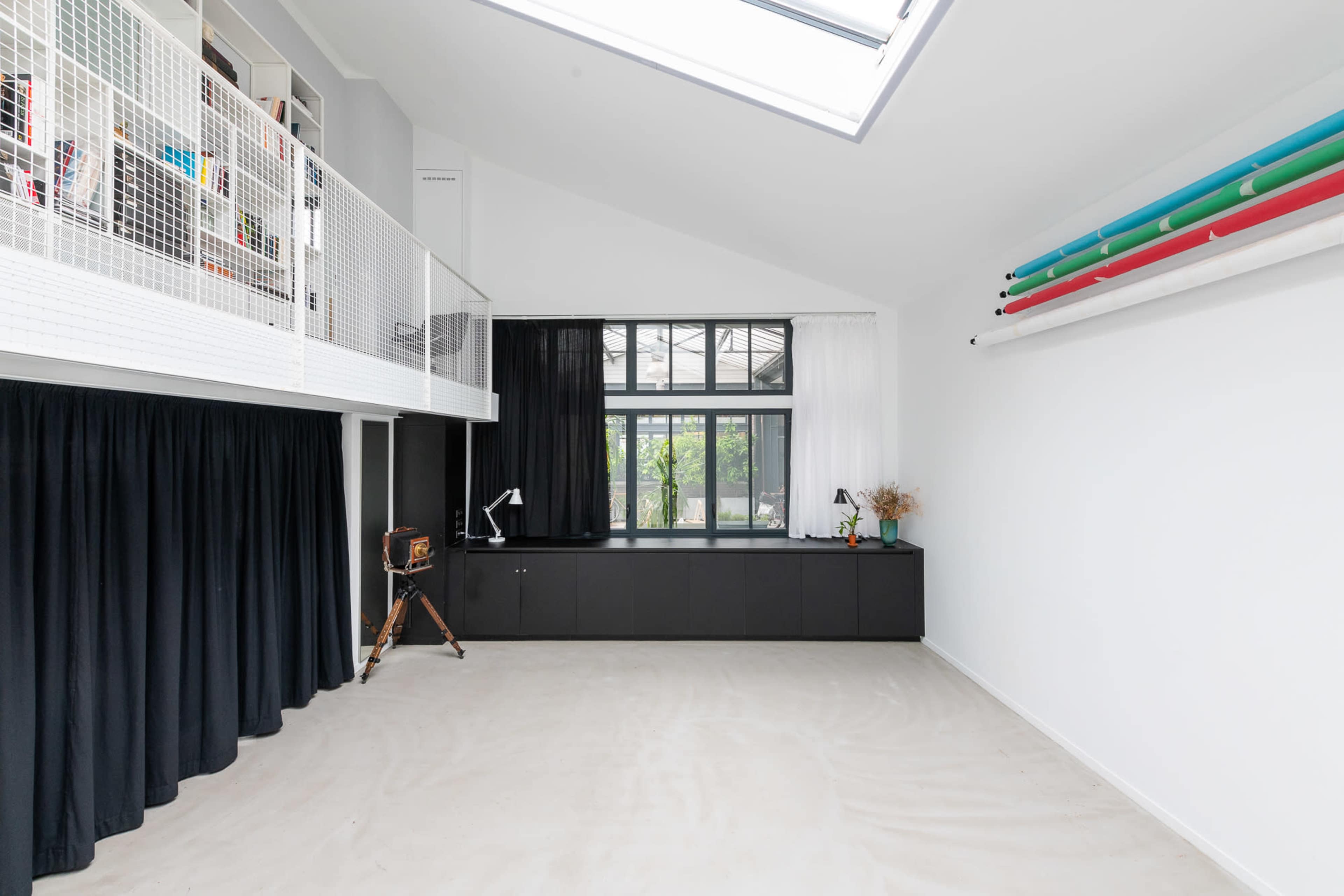 A spacious, modern interior with a high ceiling, large windows, and a mezzanine level, featuring minimalistic furniture and natural light.