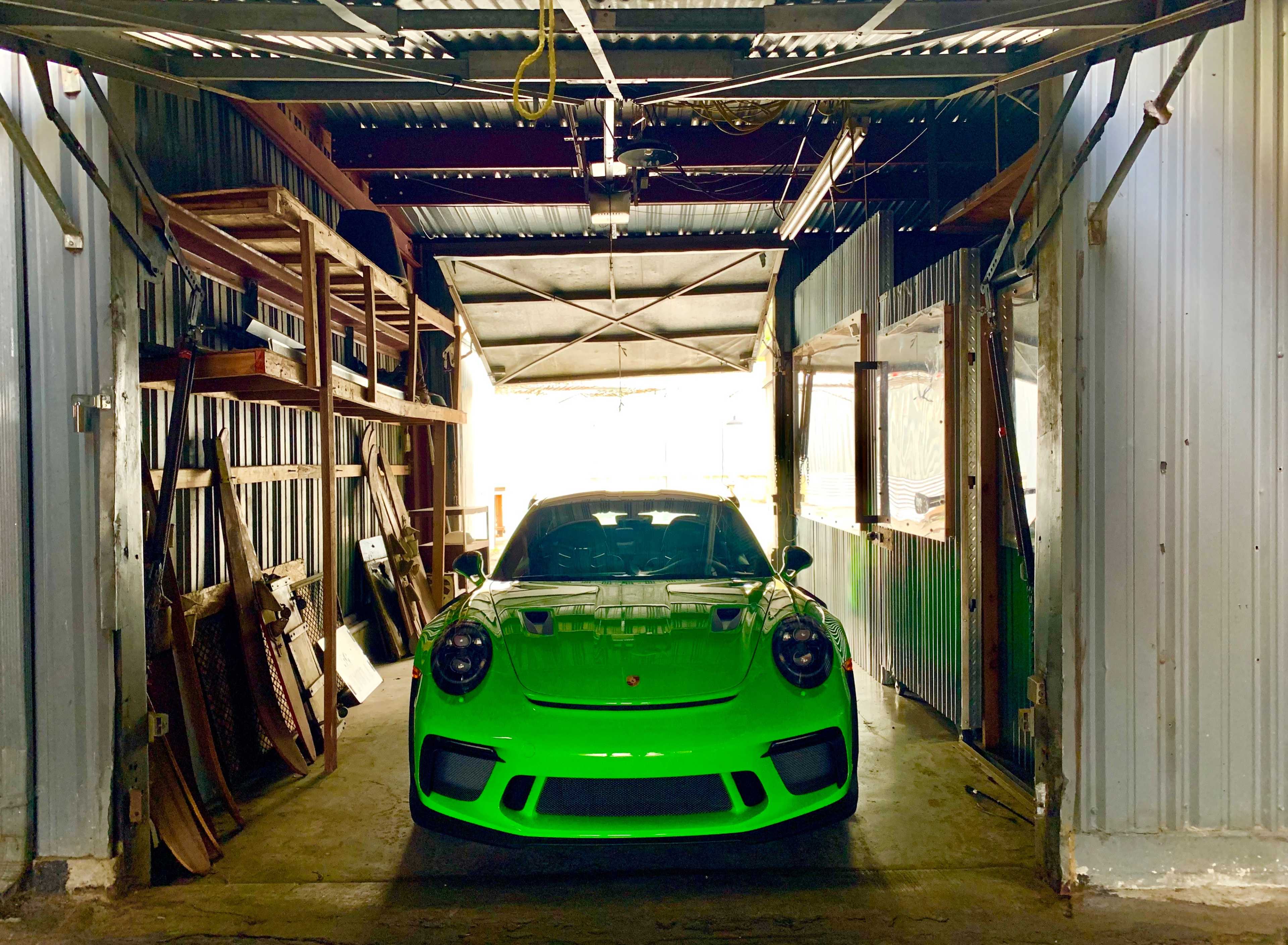 A bright green sports car is parked in a warehouse with open access on both sides.