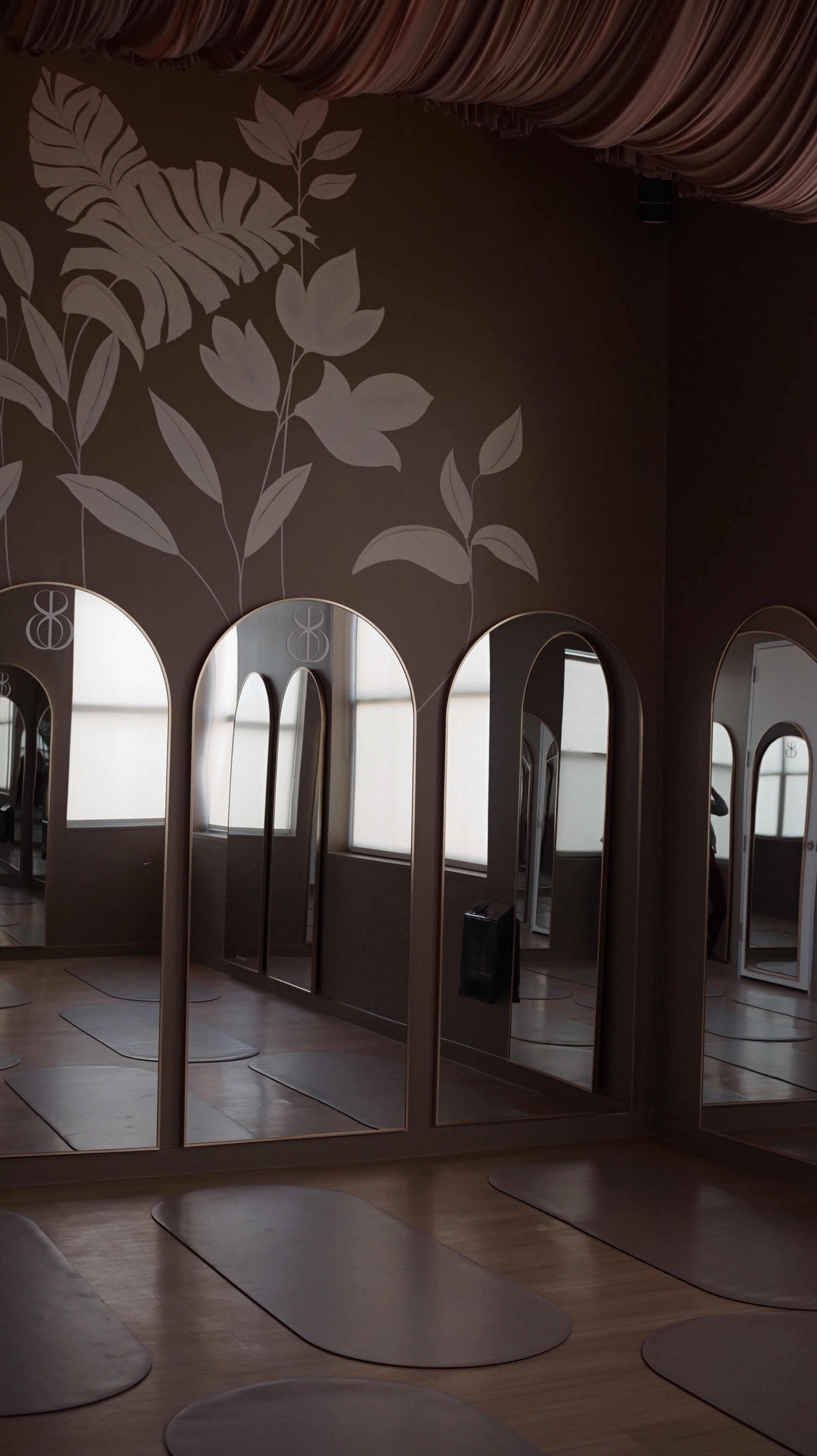 The image depicts a yoga studio with arched mirrors reflecting a minimalist interior and floral wall decorations.