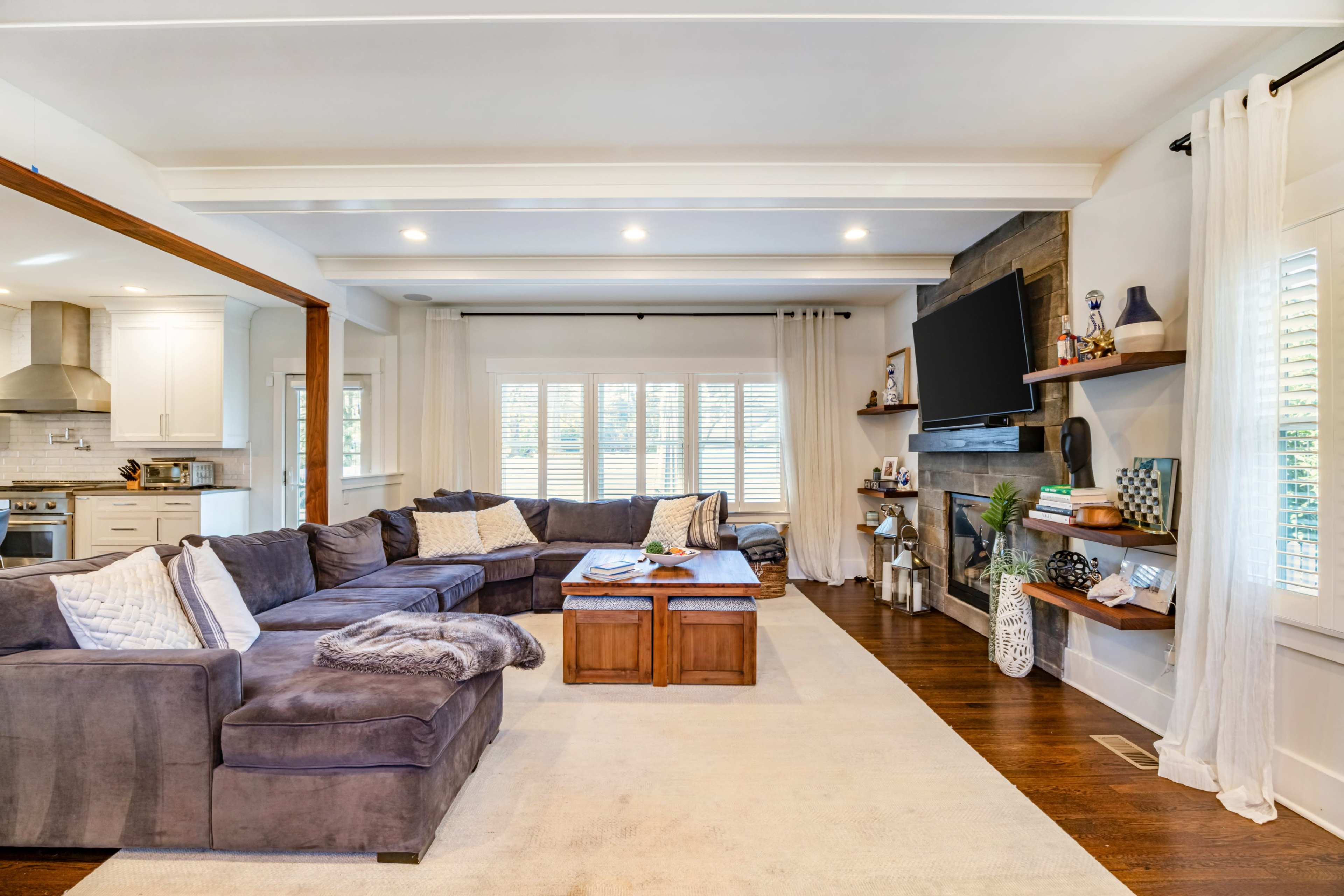 The image shows a spacious living room with a large sectional sofa, a wooden coffee table, and a mounted television above a decorative wall.