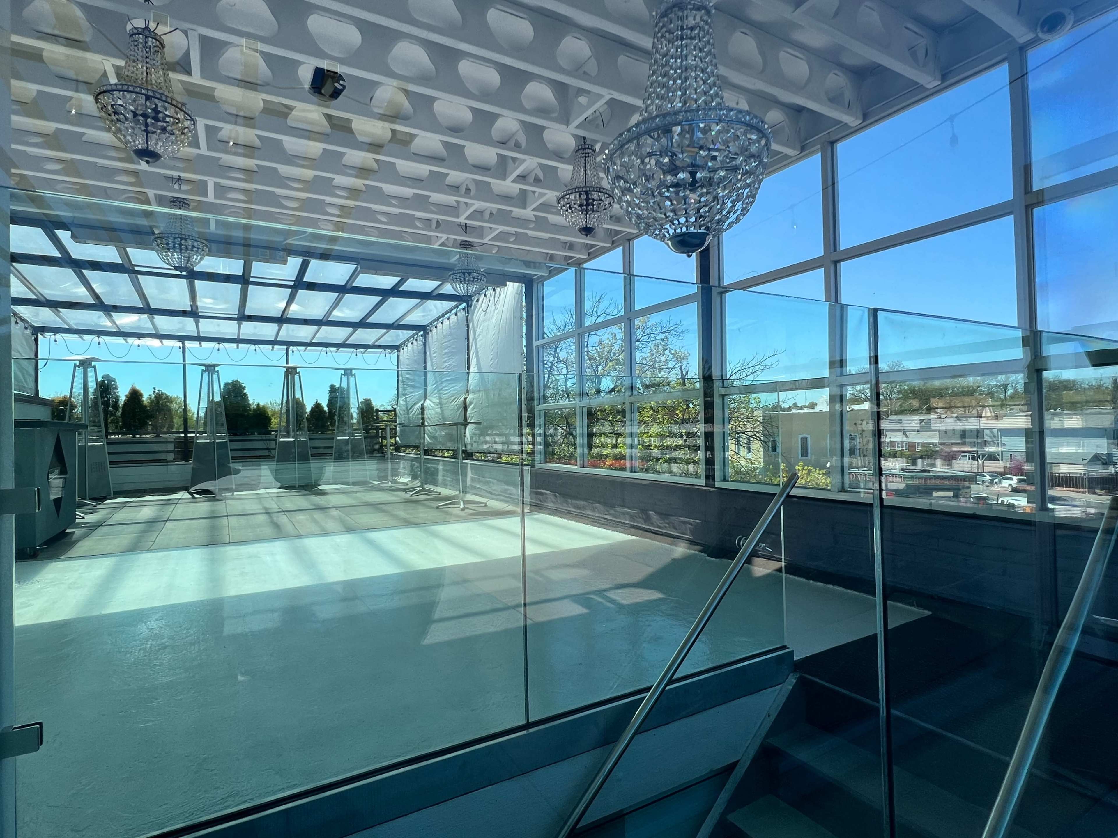 A large, well-lit room with glass walls and chandeliers, empty except for the light streaming in through the windows.