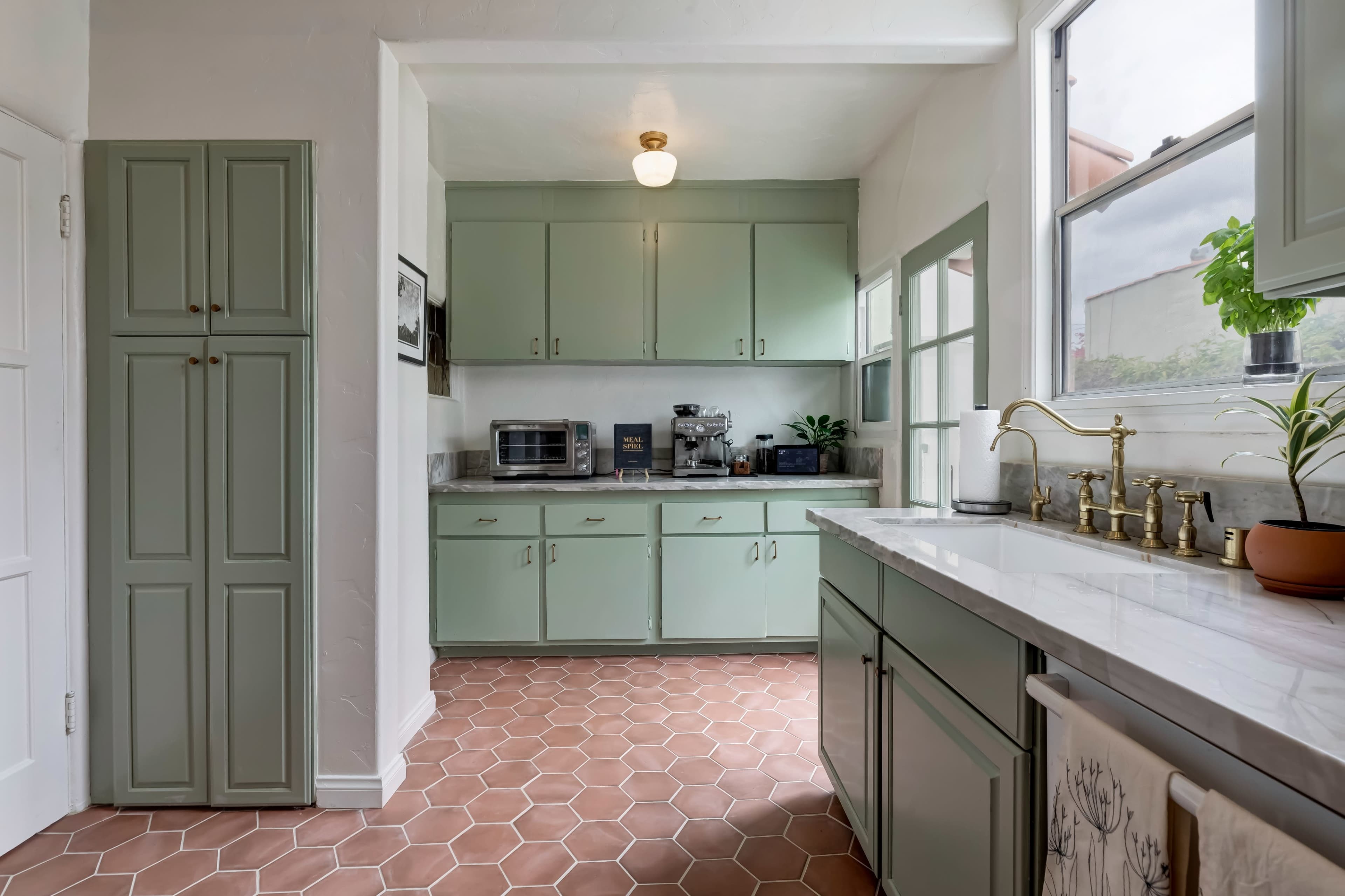A modern kitchen features mint-green cabinetry, a marble countertop, and hexagonal tile flooring.
