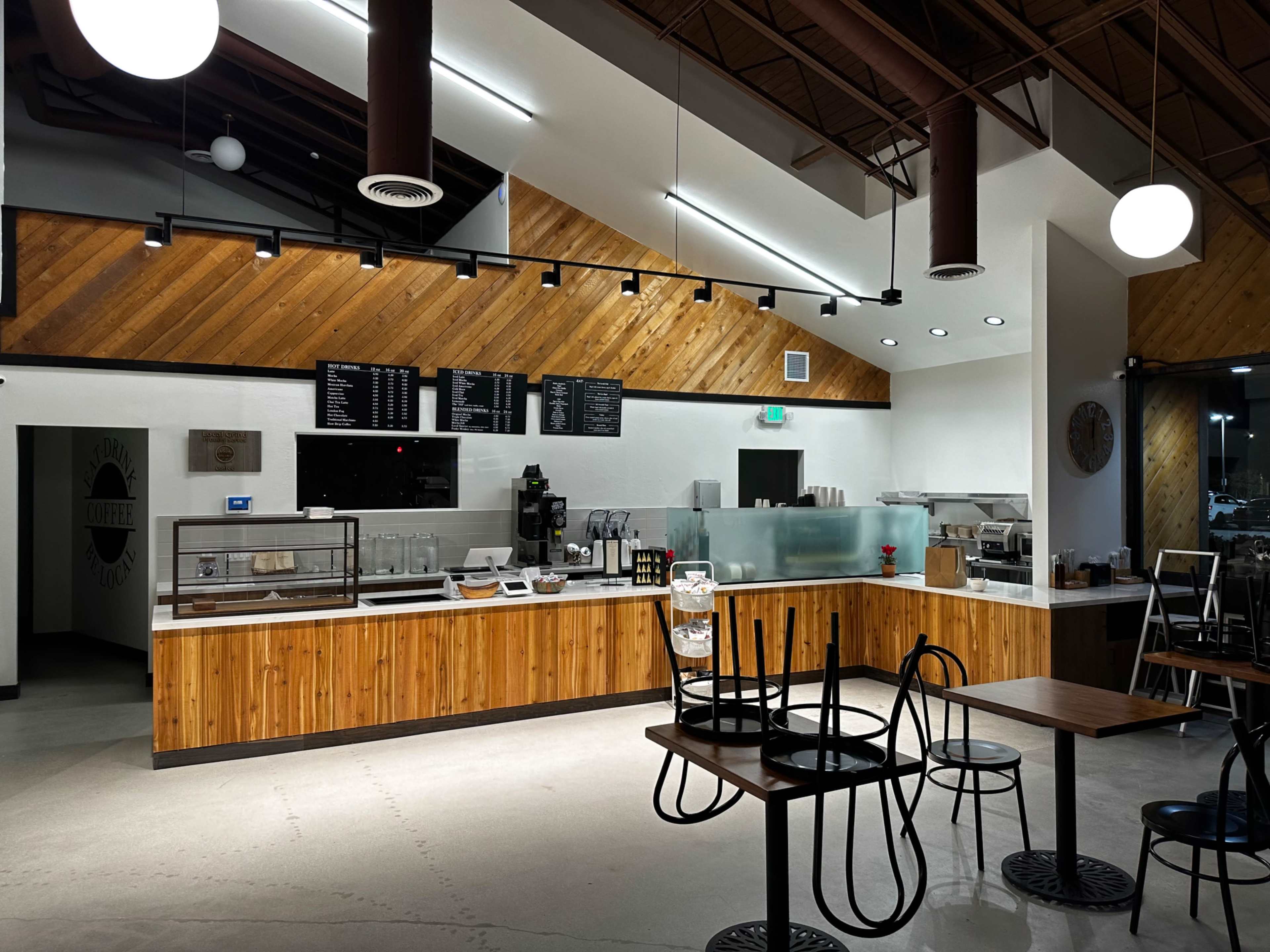 A modern, dimly lit café interior with wooden accents, a service counter, and several empty tables and chairs.