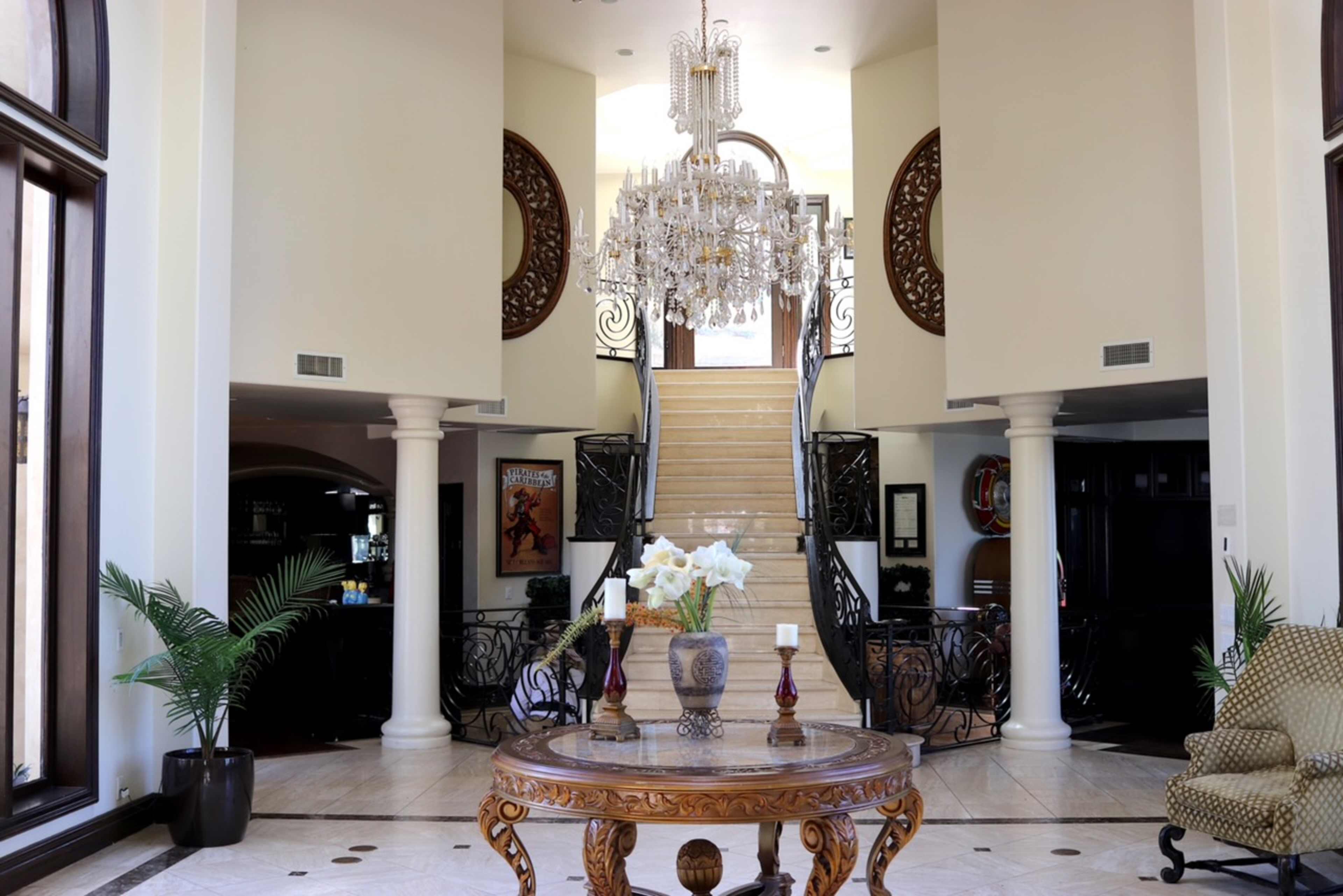 A grand foyer with a chandelier, a staircase, and a circular table adorned with flowers.