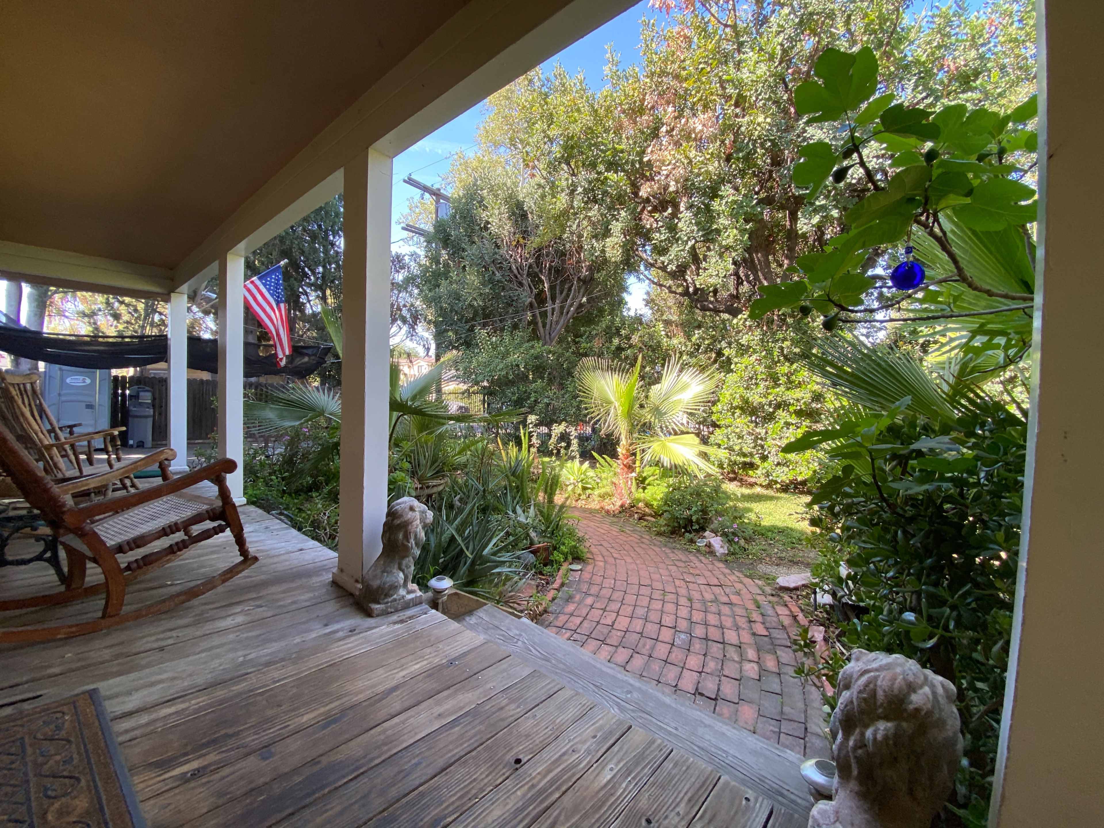 A porch with rocking chairs overlooks a brick path leading through a lush garden with palm trees and greenery.