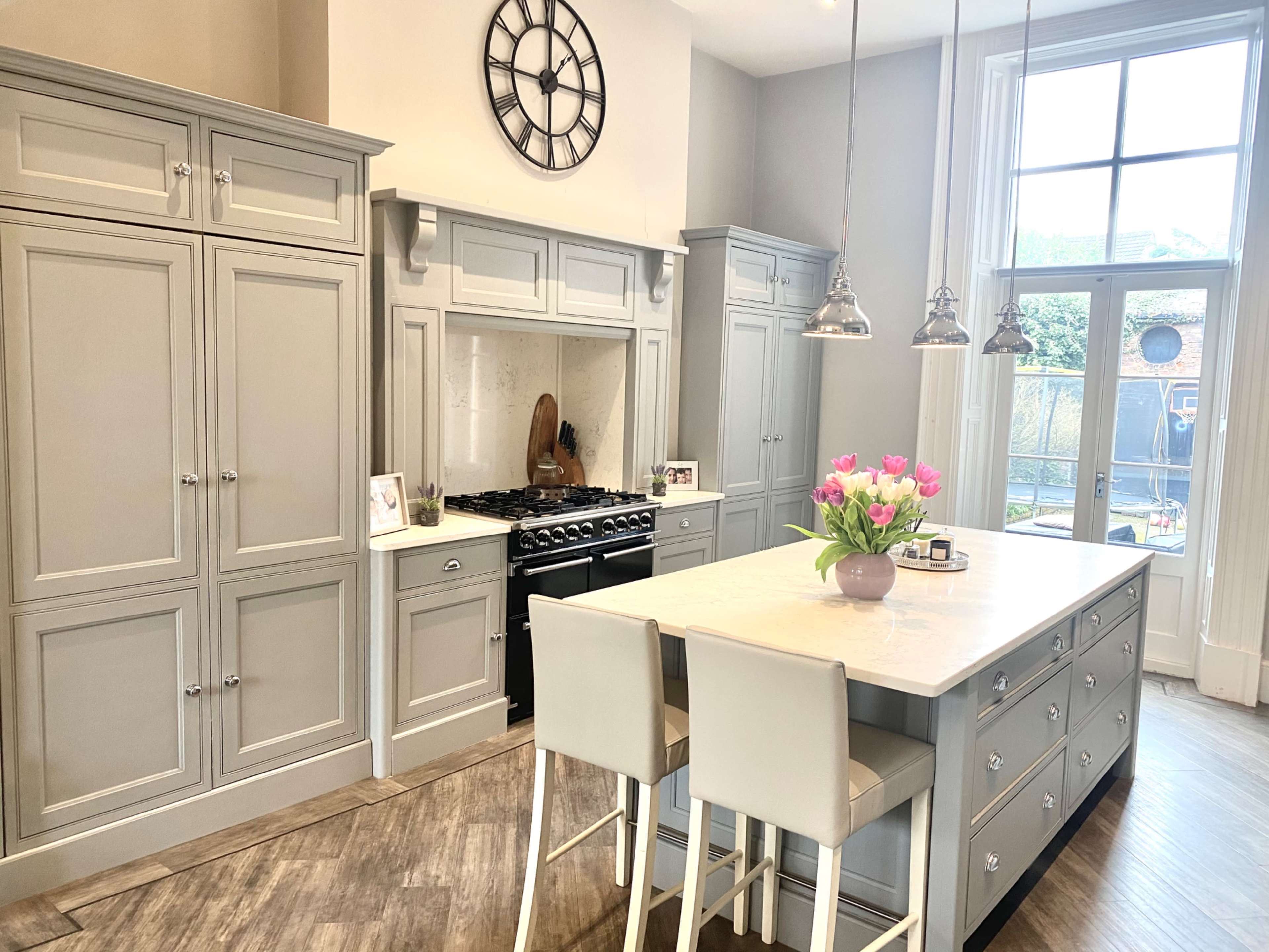 A modern kitchen features gray cabinetry, a gas range, a large island with seating, and a window overlooking an outdoor space.