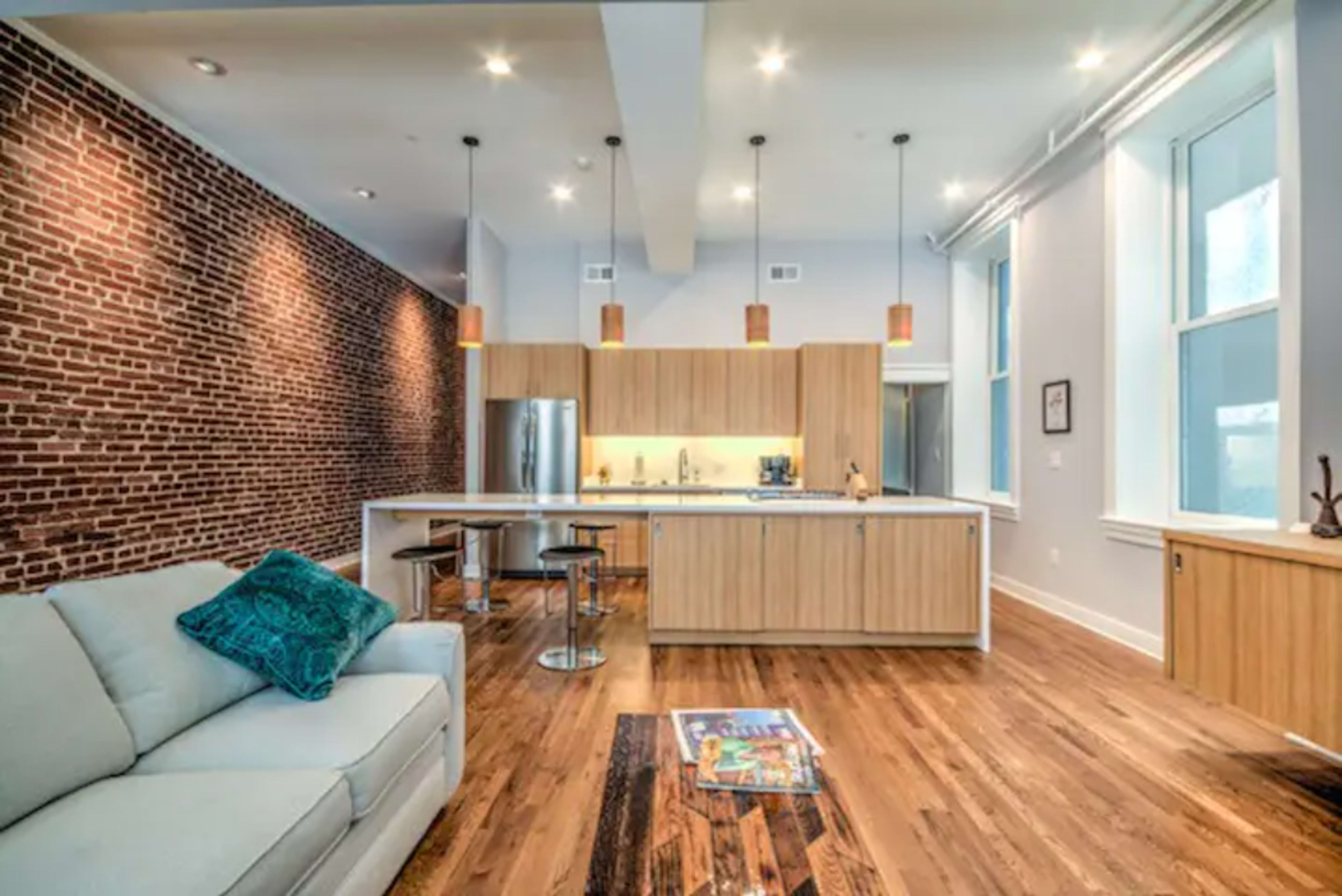 A modern kitchen and living area with exposed brick walls, wooden cabinetry, and a comfortable couch.