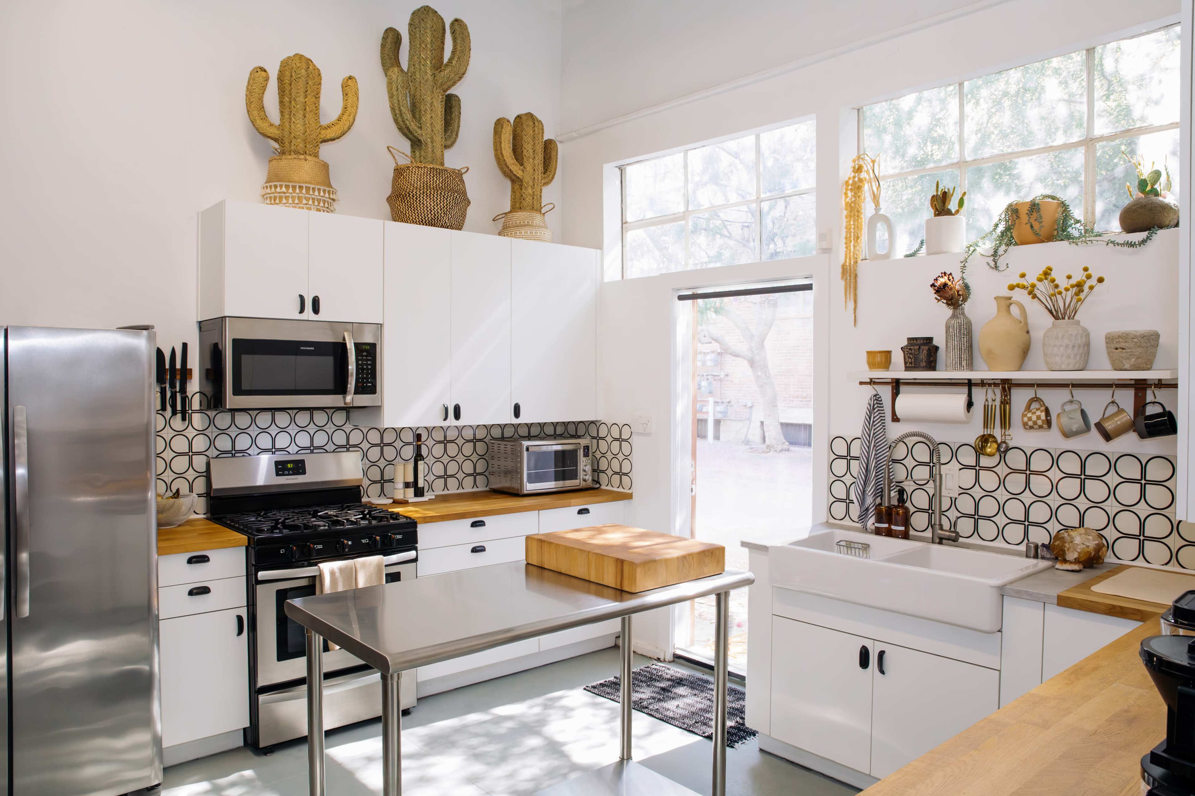A modern kitchen with white cabinetry, a stainless steel refrigerator, a gas stove, and decorative cacti displayed above the cabinets.