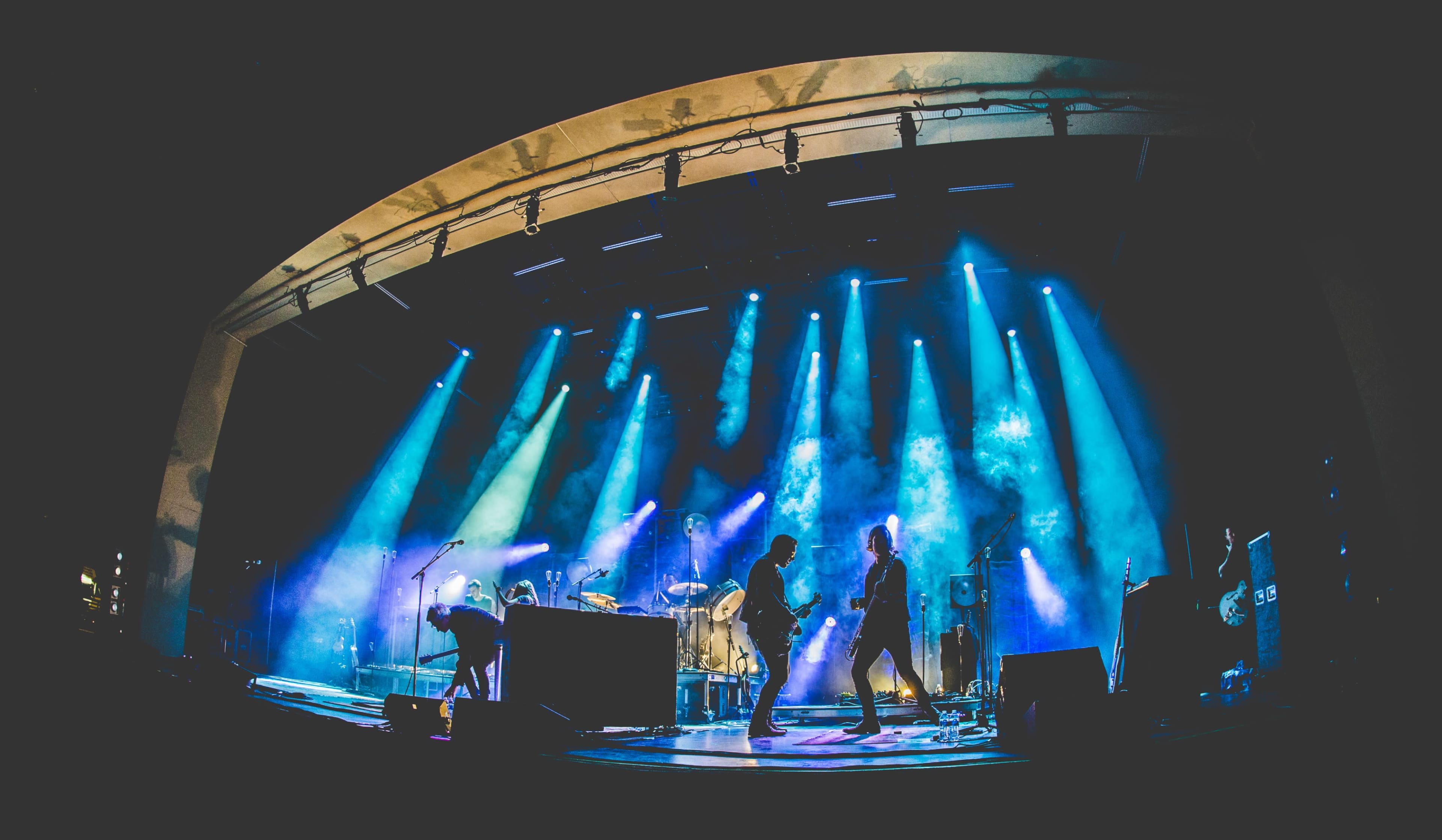 A band performs on stage under a vibrant display of blue and green lighting with smoke effects.