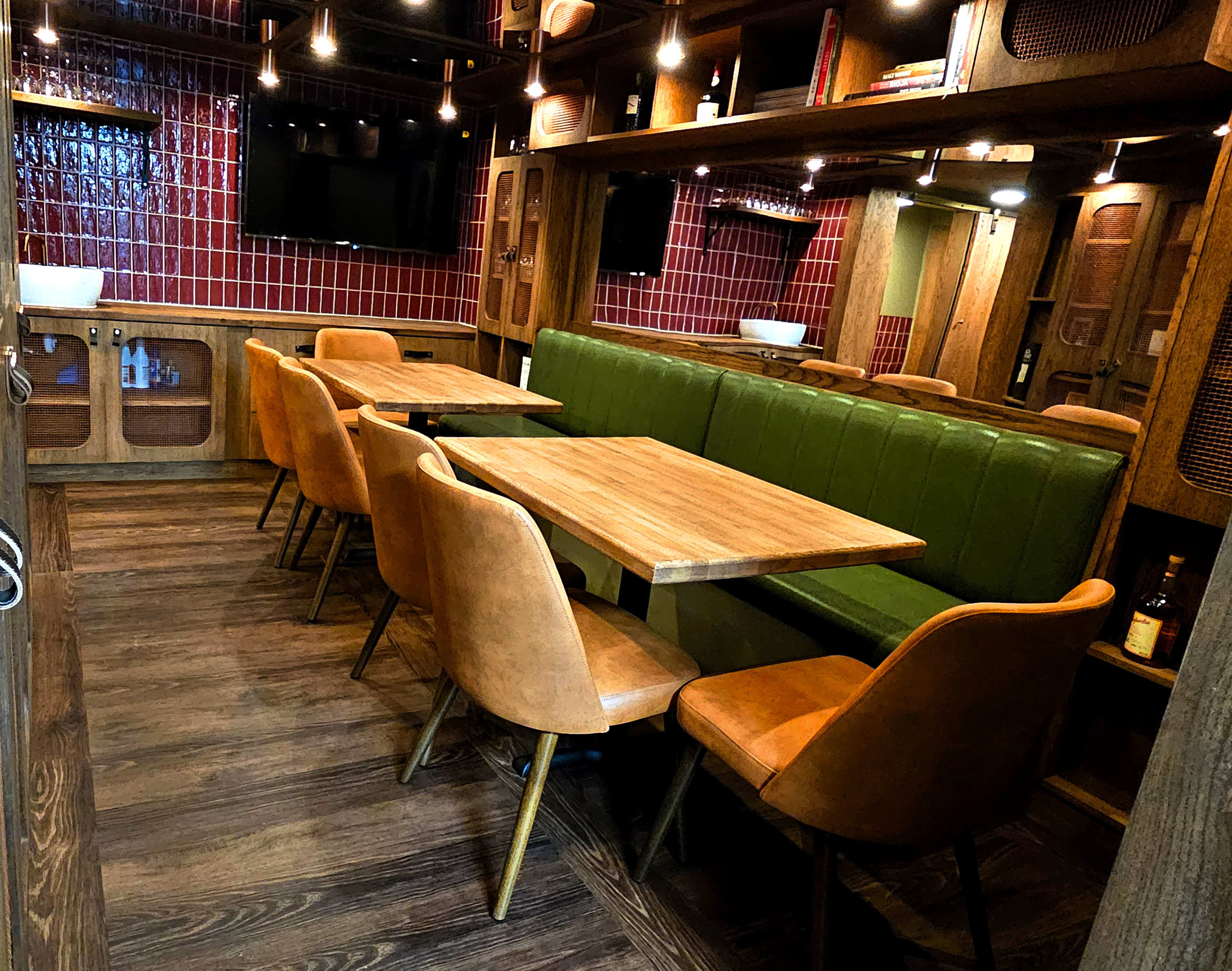 The image shows a cozy restaurant interior featuring wooden tables and green upholstered seating, illuminated by pendant lights.