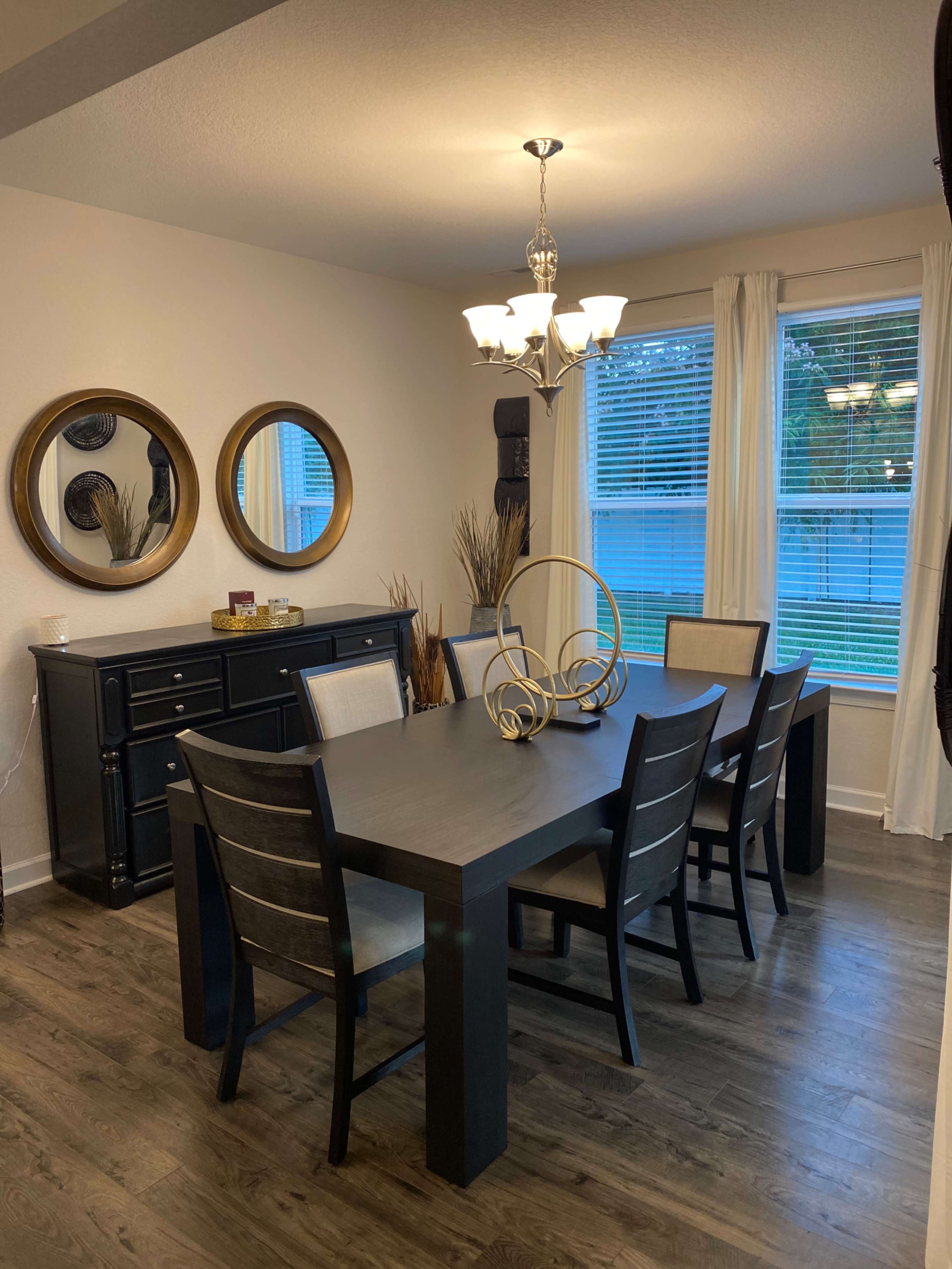 The dining room features a dark wood table surrounded by six chairs, with a chandelier overhead and mirrors on the wall.