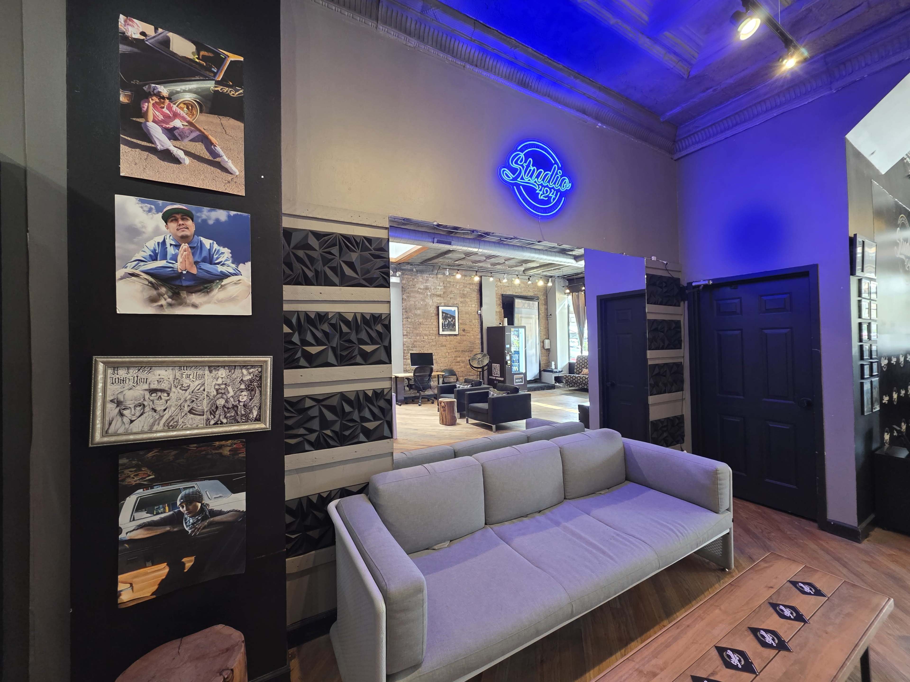 The image shows a modern room featuring a gray sofa, artwork on the walls, and a neon sign illuminating the space.