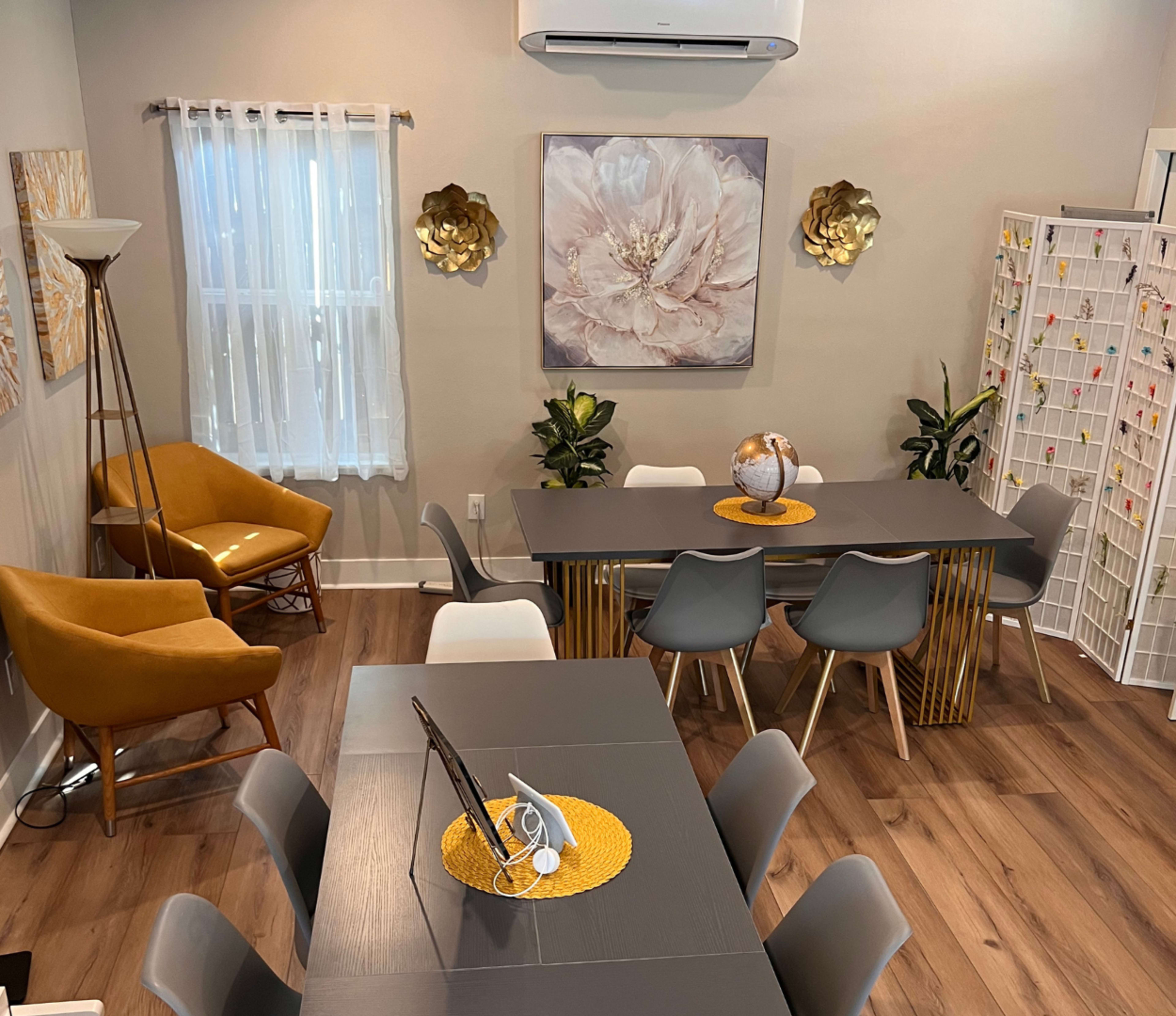 A modern, well-lit meeting room with a large table, several chairs, decorative plants, and artwork on the walls.