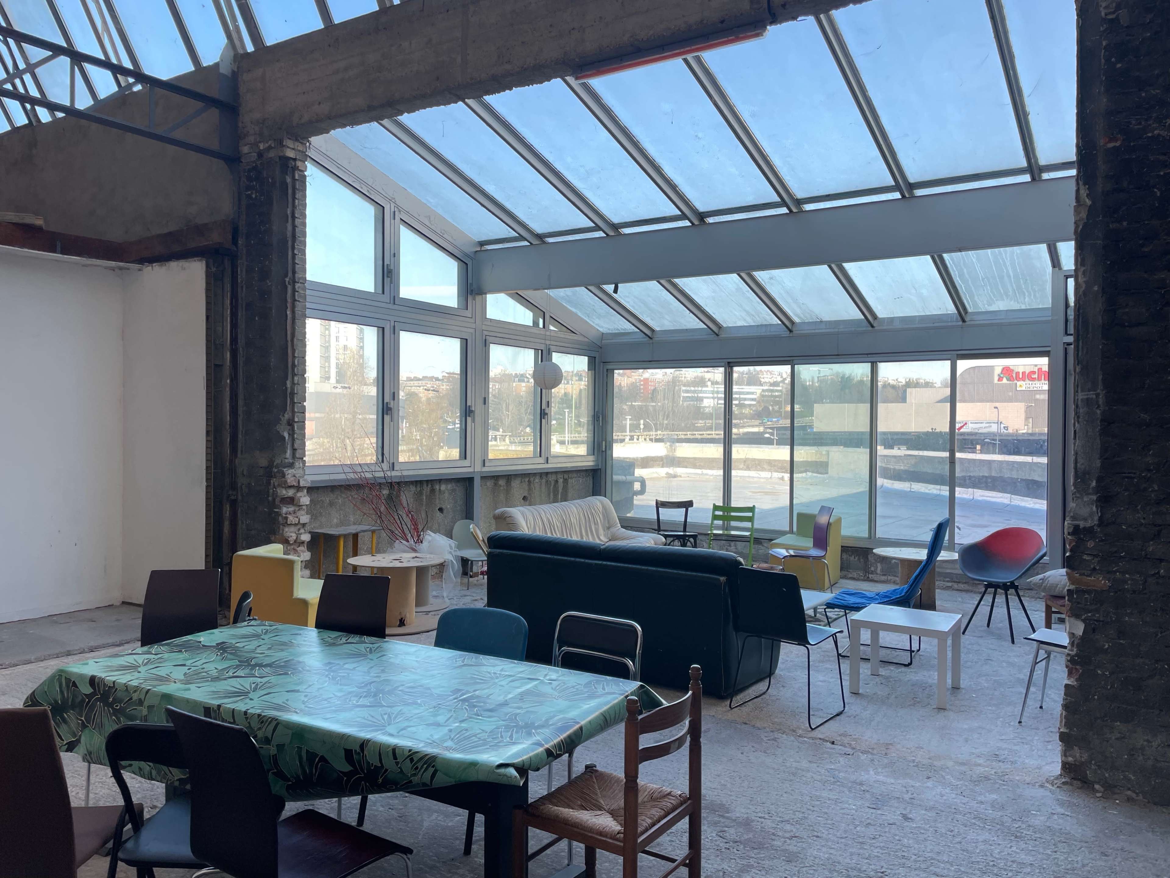 An indoor space with large windows, featuring a mix of furniture including tables, chairs, and couches.