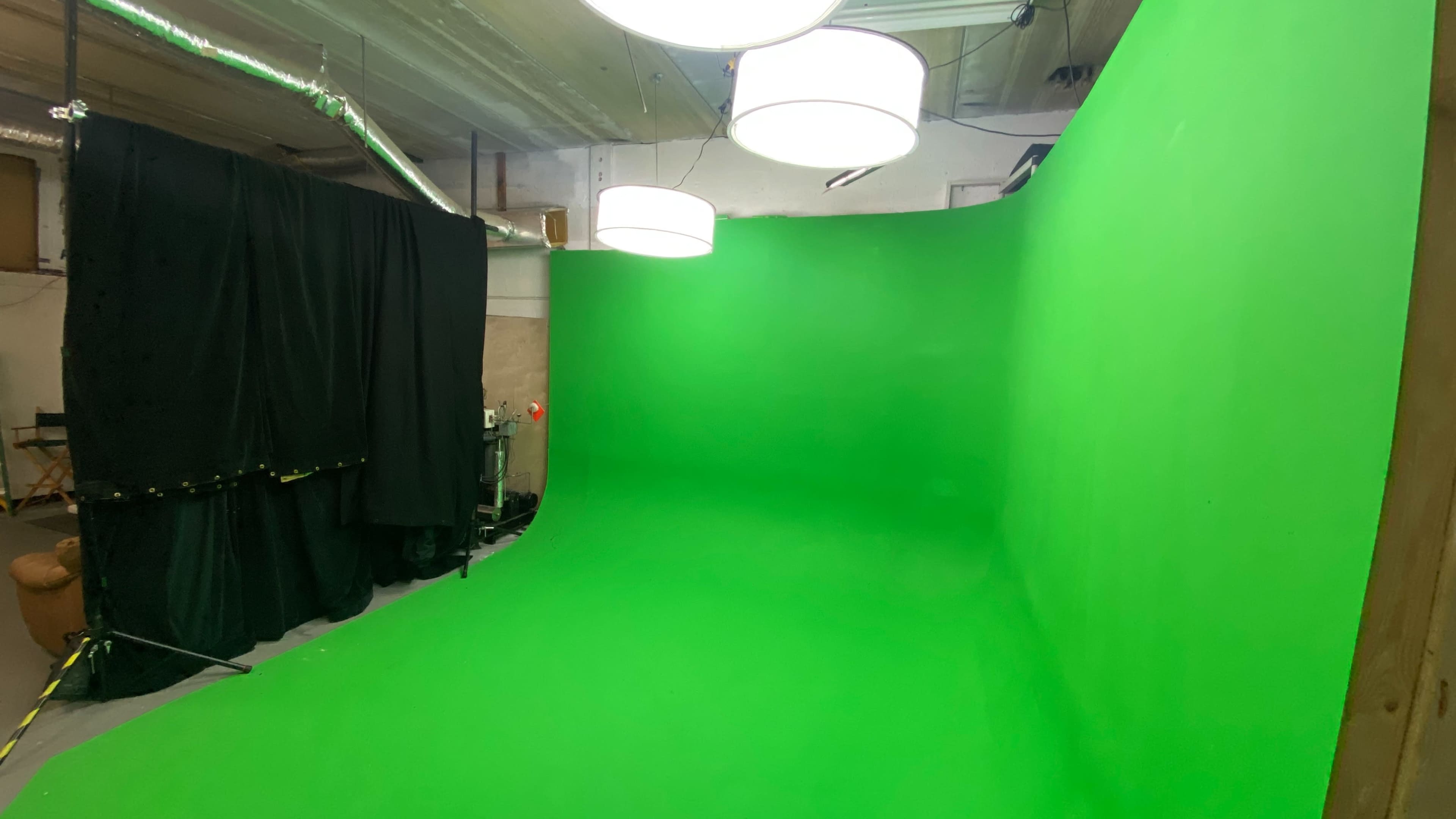 A green screen setup in a studio with black drapes and pendant lights overhead.