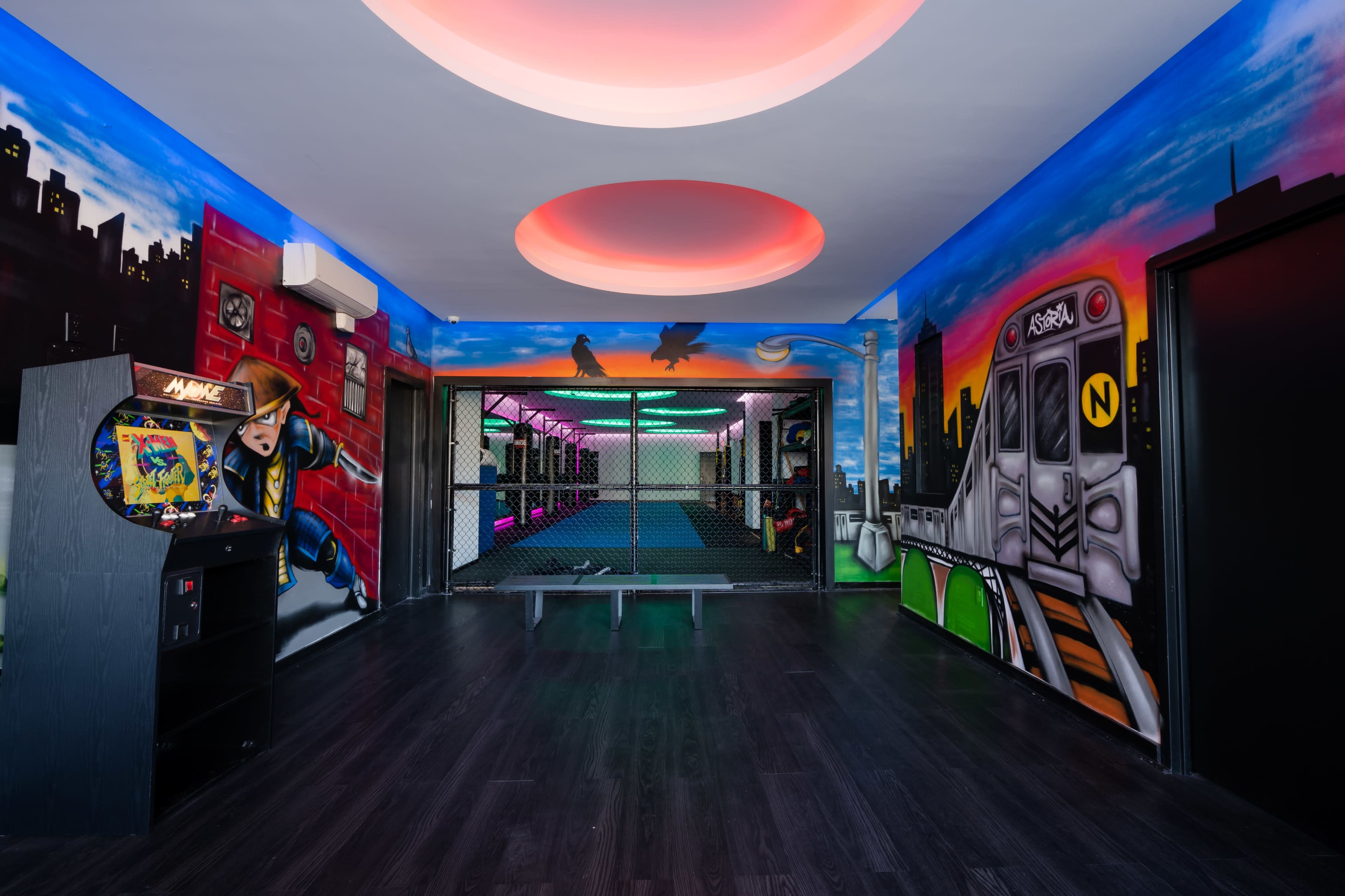 A brightly painted indoor space with colorful murals, featuring a fenced-off area and an arcade game machine in one corner.