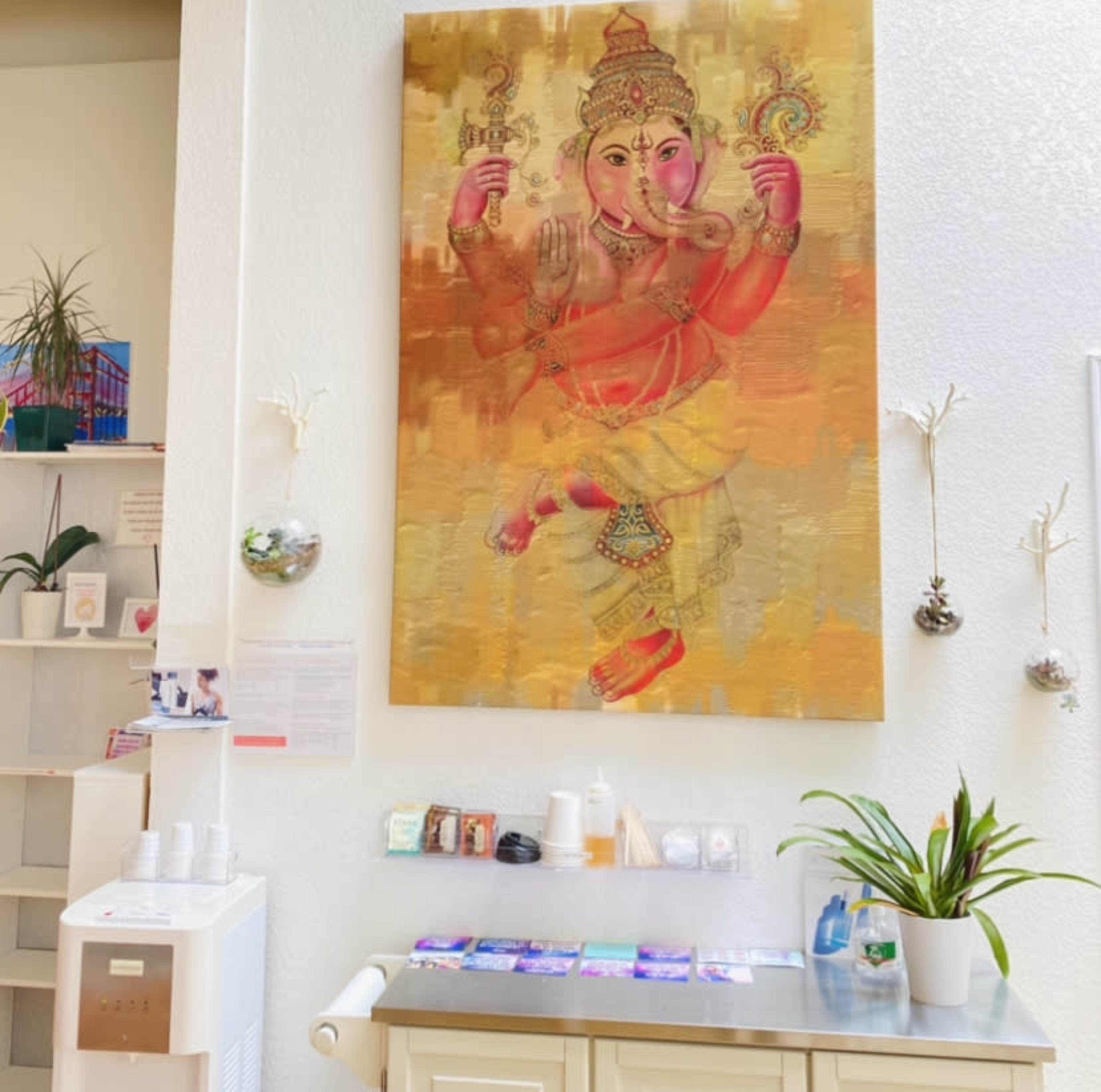 A wall adorned with a large painting of the Hindu deity Ganesha, accompanied by a table with various items, including a potted plant and neatly arranged products.