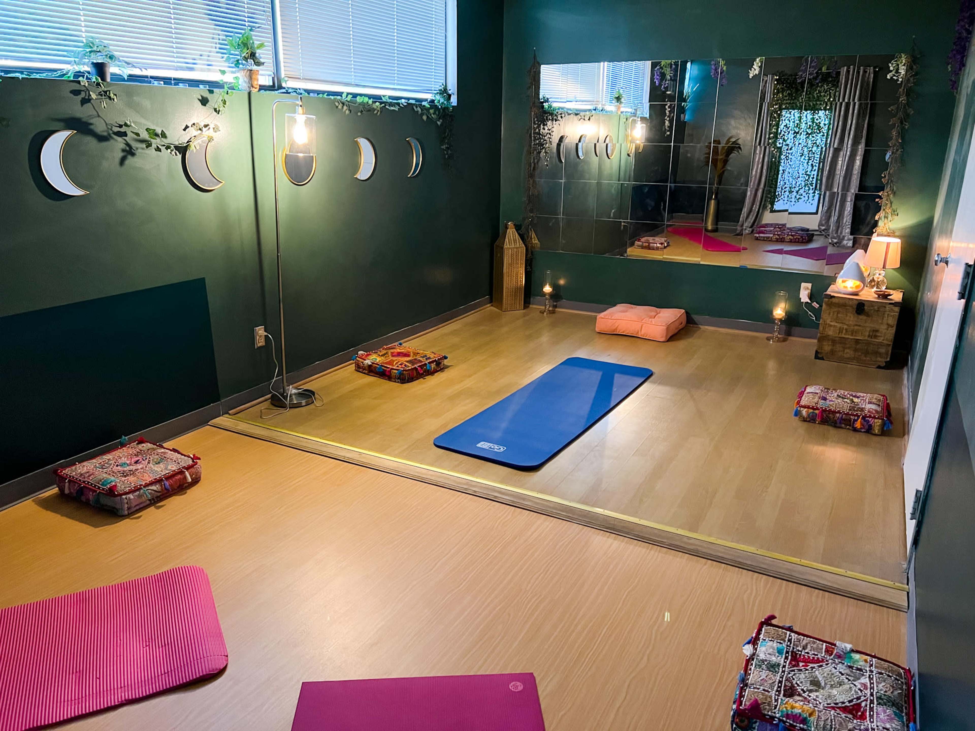 The image shows a serene yoga studio featuring mats, cushions, and soft lighting, with decorative elements on the walls and a mirror reflecting the space.