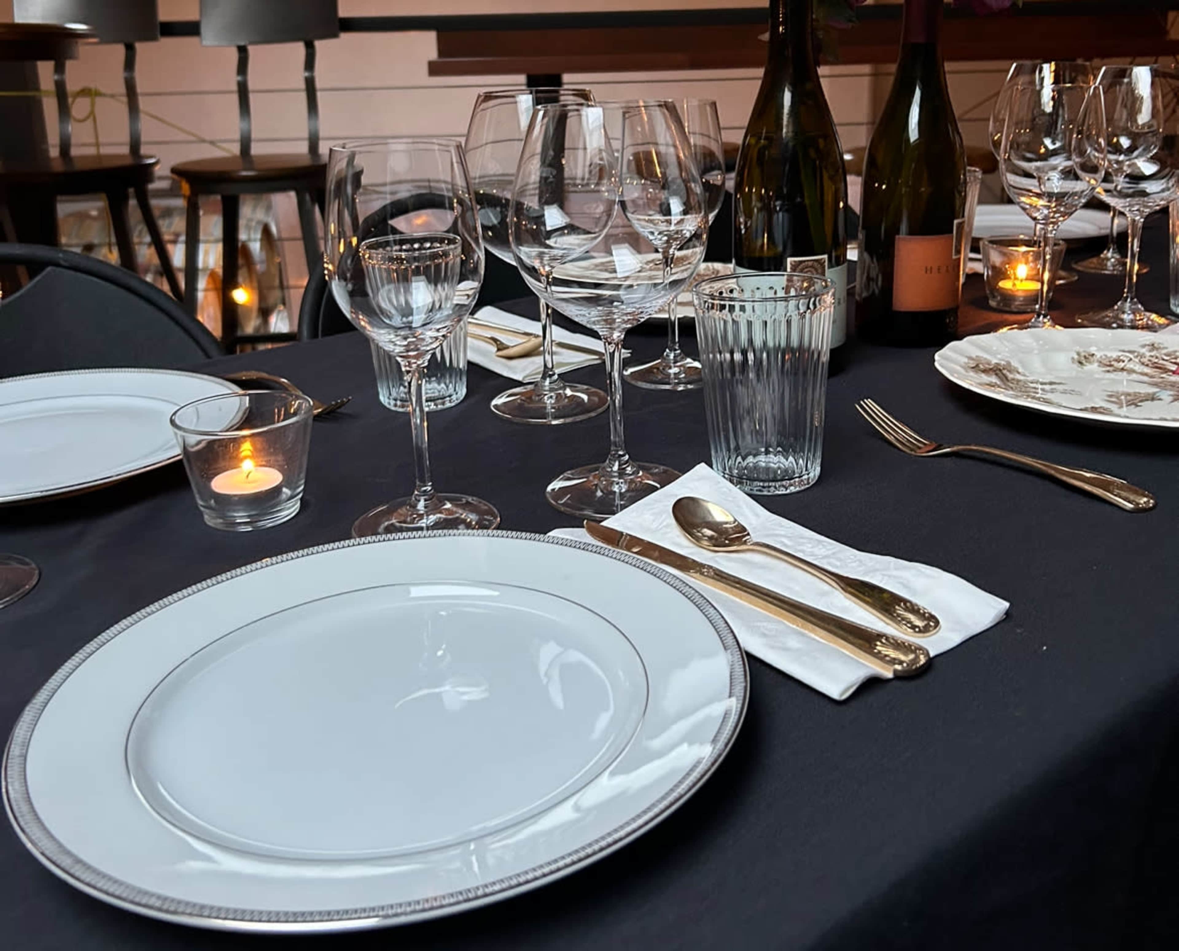 A dining table is set with elegant white plates, various glassware, silver utensils, and candlelight.