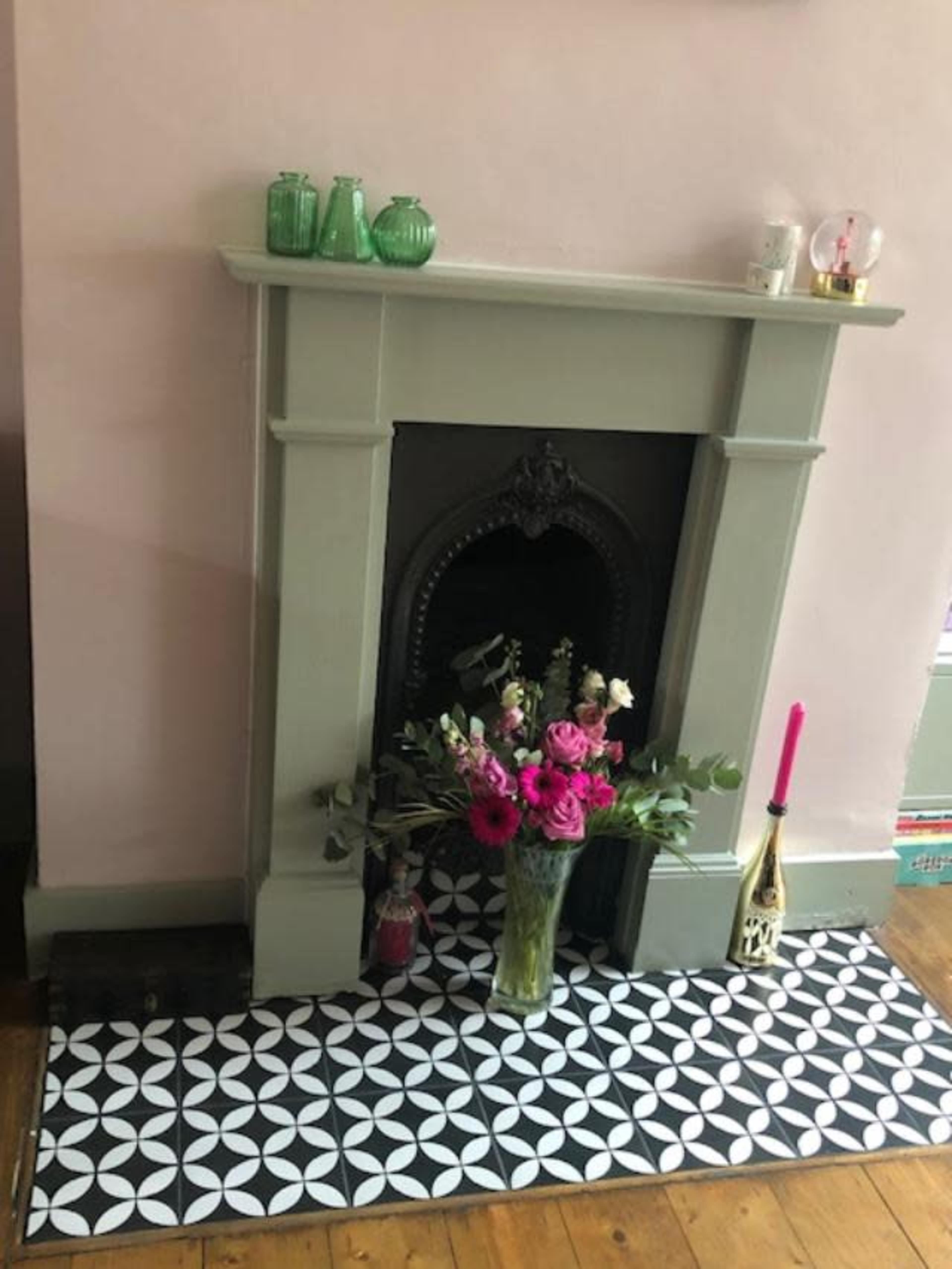 A decorative fireplace with a green mantle, adorned with a bouquet of flowers and a colorful rug featuring a geometric pattern.