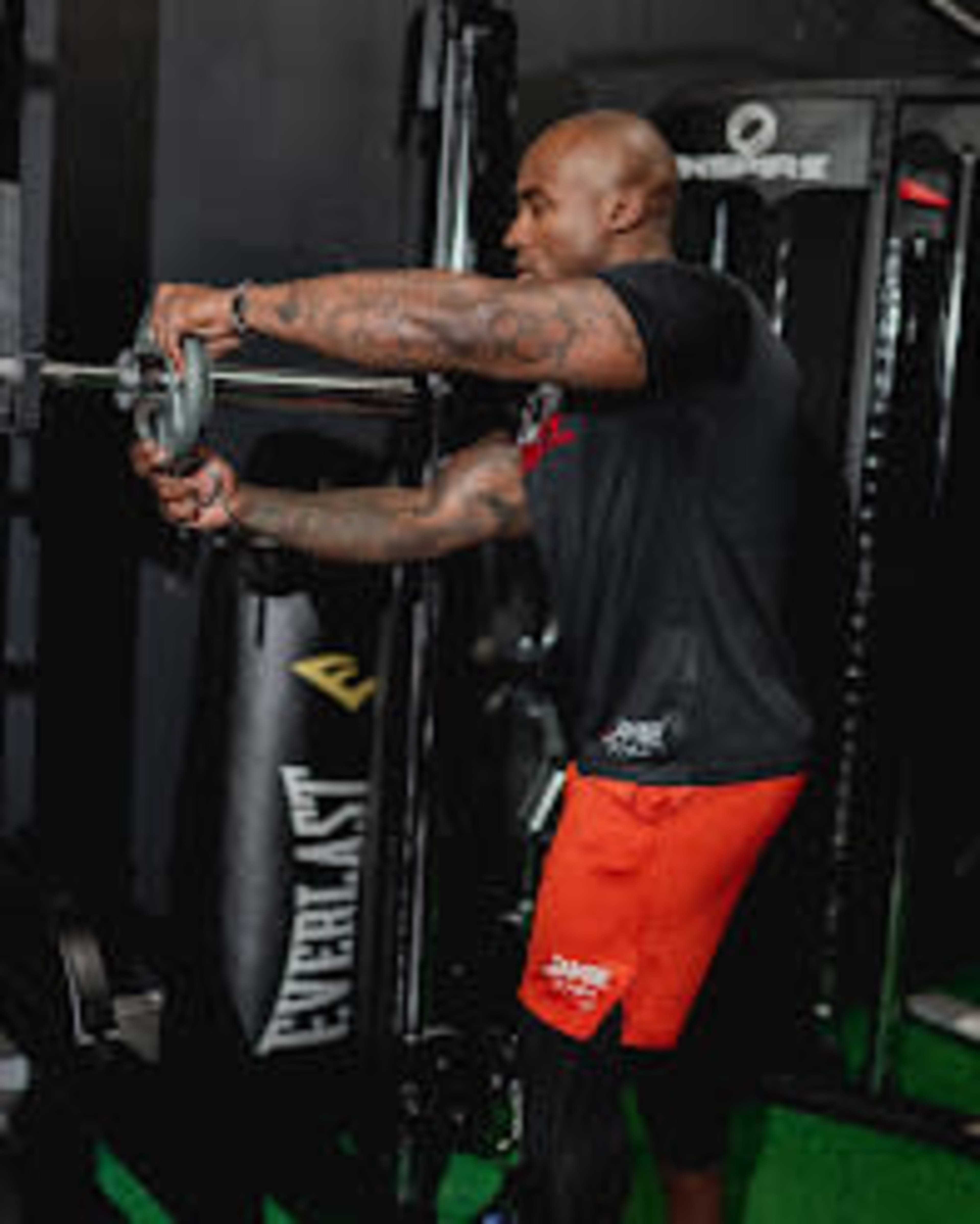 A person is lifting a barbell in a gym setting equipped with various exercise equipment.