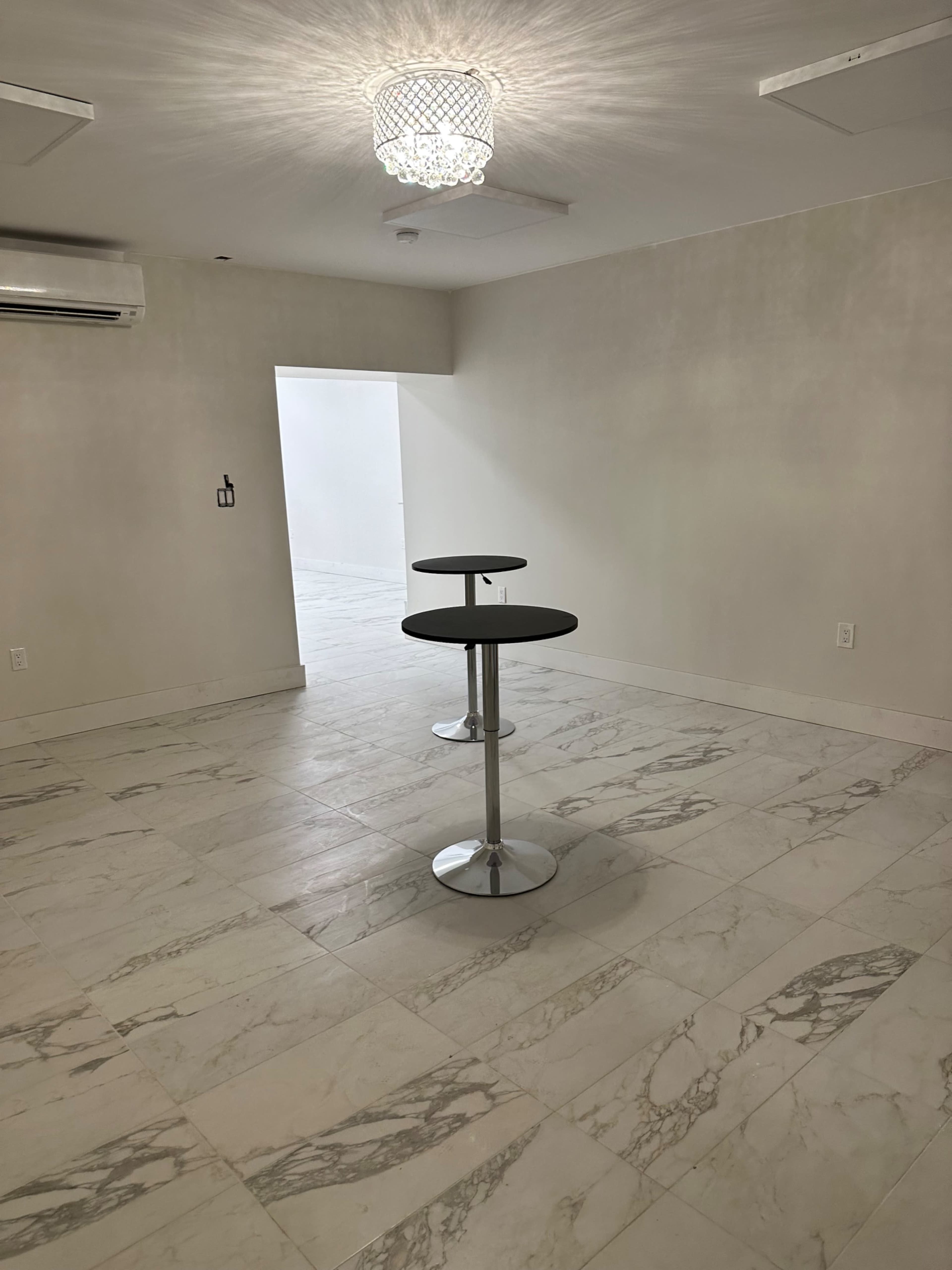 A room with two circular tables on a marble floor beneath a decorative light fixture.