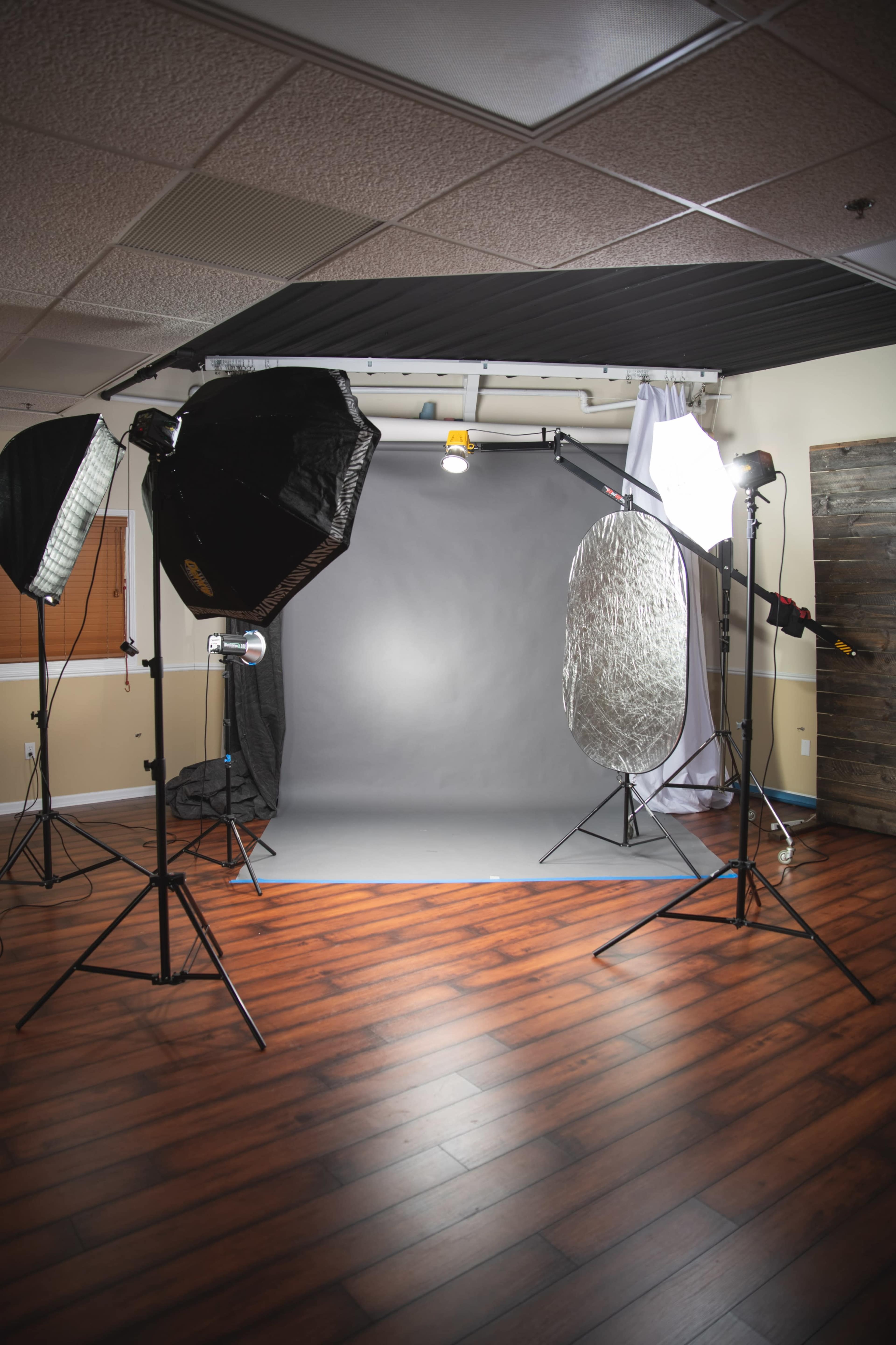 A photography studio setup with lighting equipment, a gray backdrop, and reflectors arranged on a wooden floor.