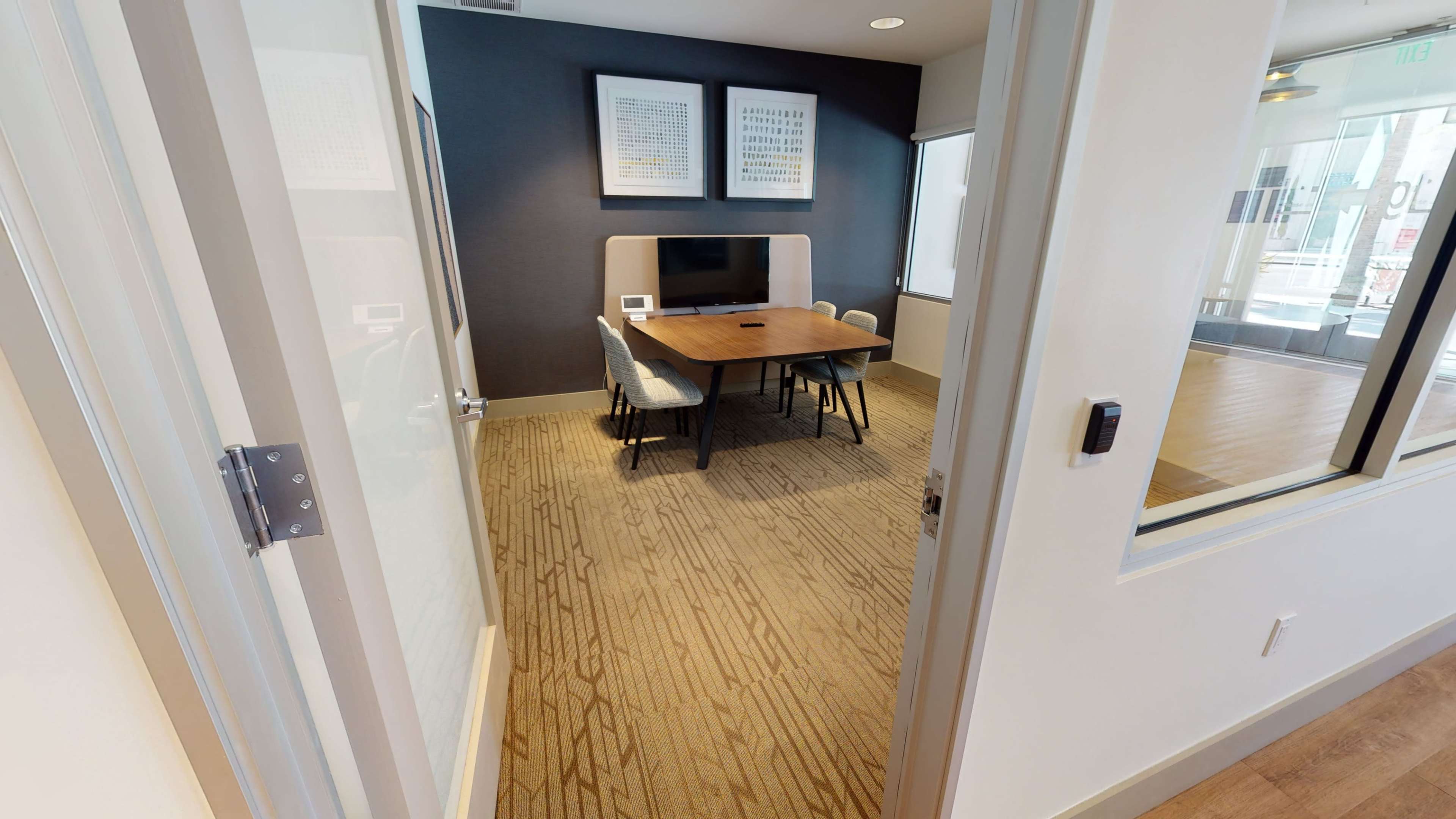 A conference room with a wooden table and chairs is visible through an open doorway, accompanied by a television mounted on the wall.