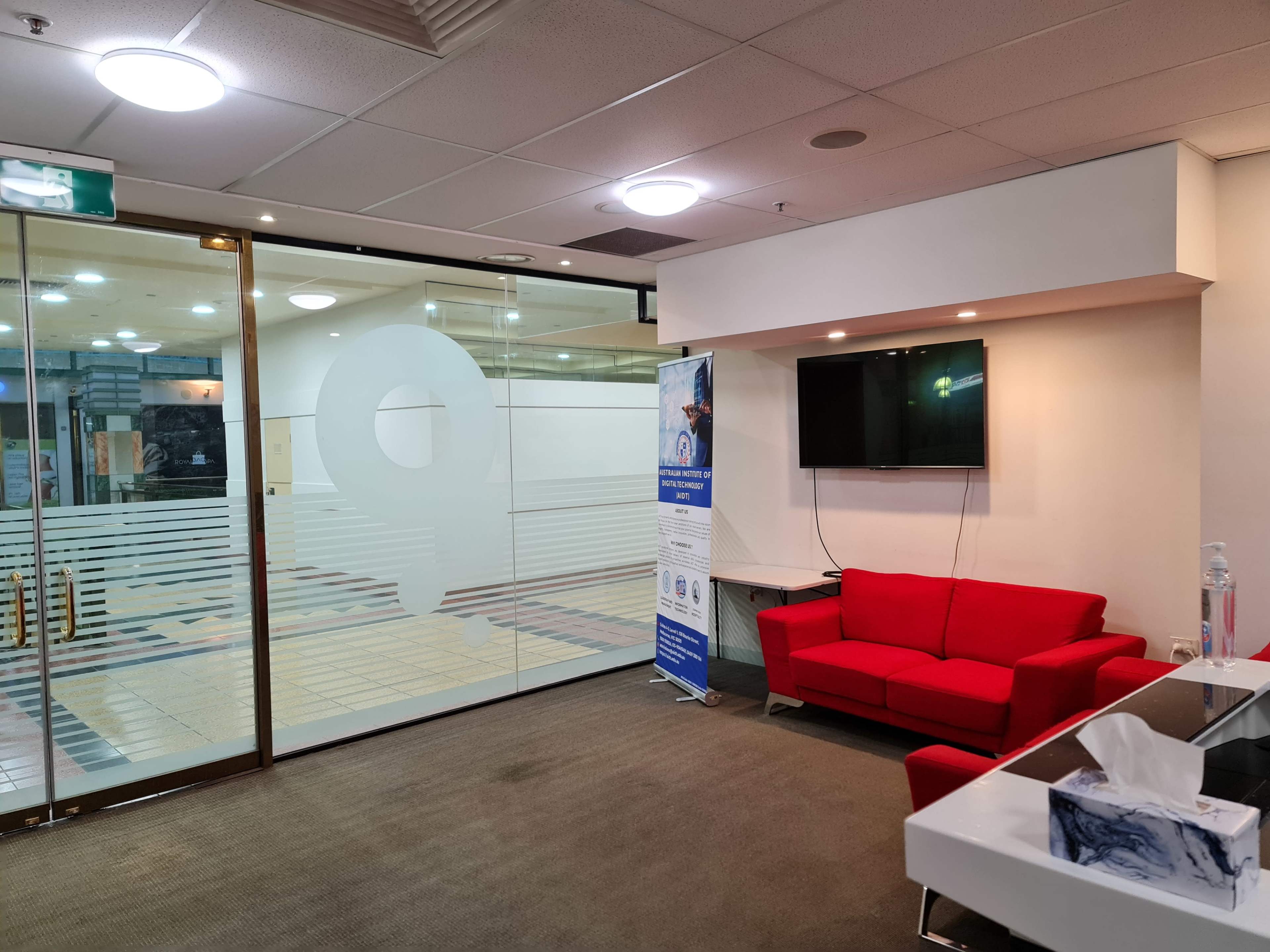 The image shows a modern office space featuring a red couch, a television mounted on the wall, and glass partitioning with a numeric design.