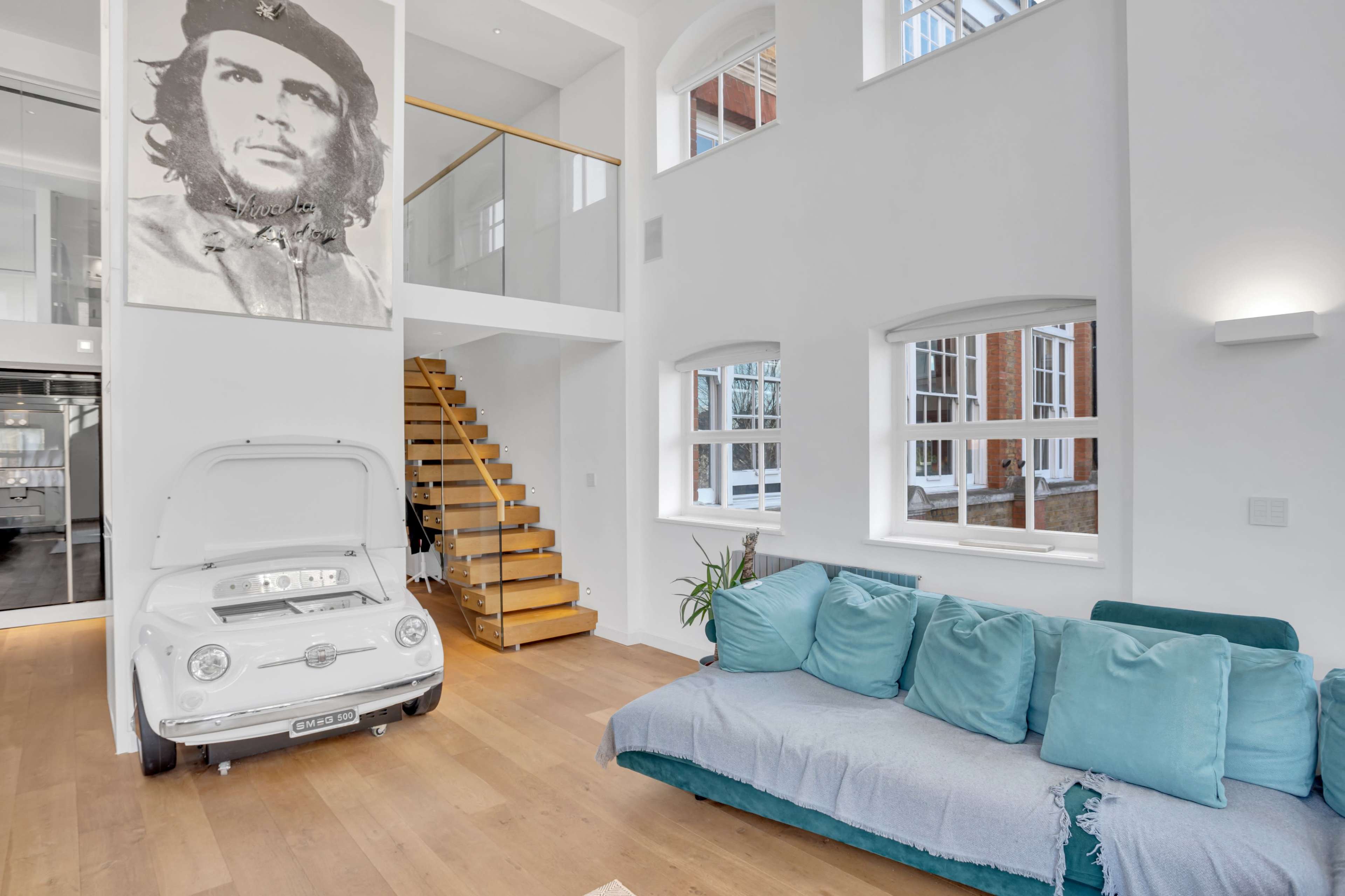 A modern living area features a blue couch, a vintage car displayed with its hood up, and a large portrait on the wall.